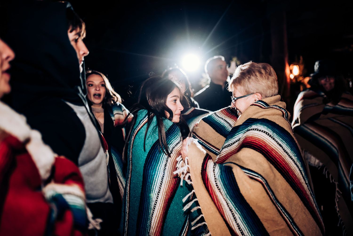 People celebrate at night while draped in colorful striped blankets.