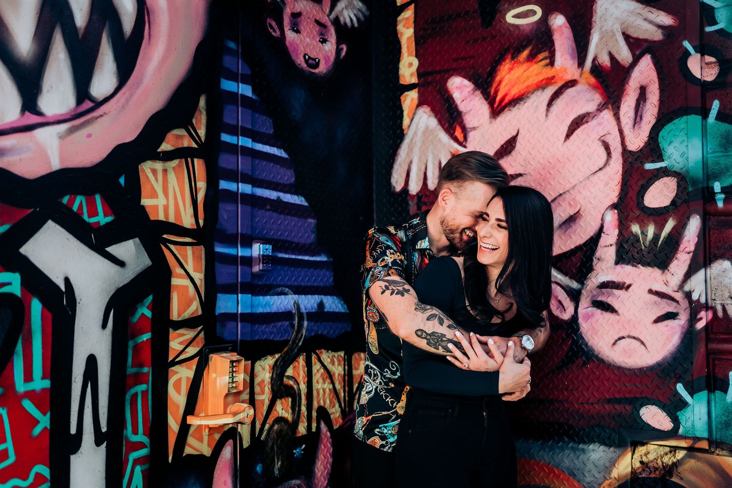 Couple poses against colorful graffiti wall in urban setting.