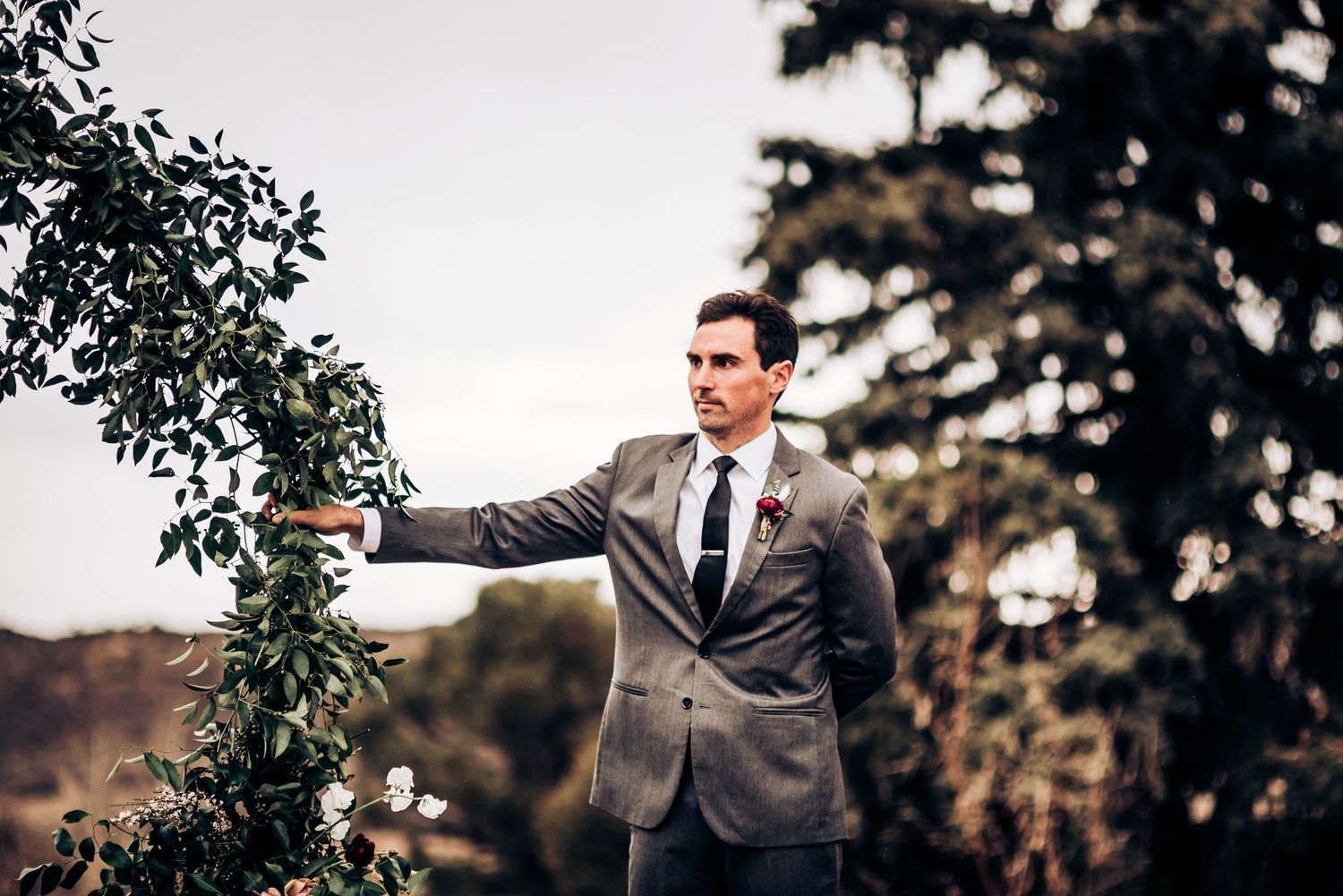 Wedding officiant gestures during ceremony beneath decorative floral arch.