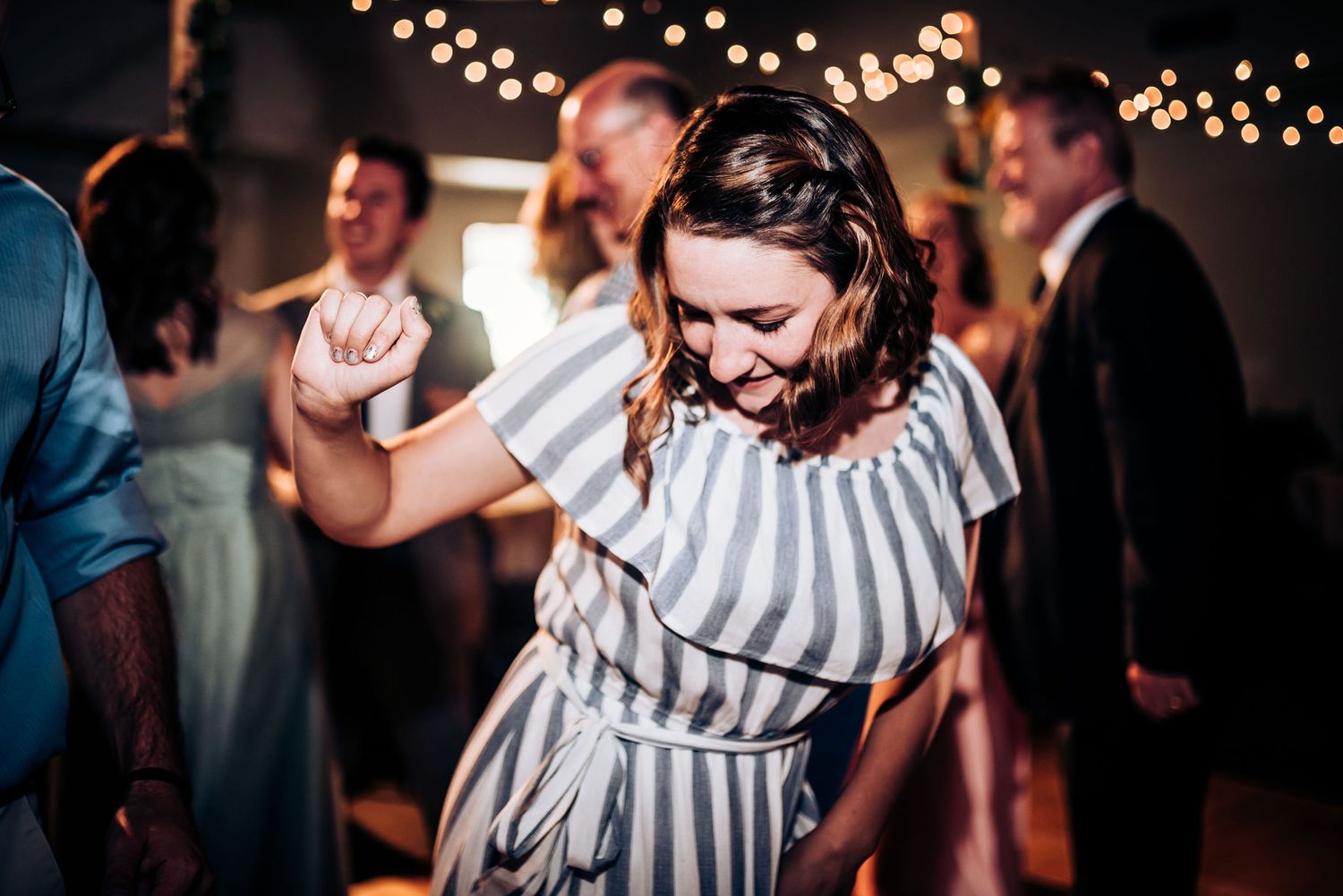 Person in striped dress dancing joyfully at indoor party with string lights in background.