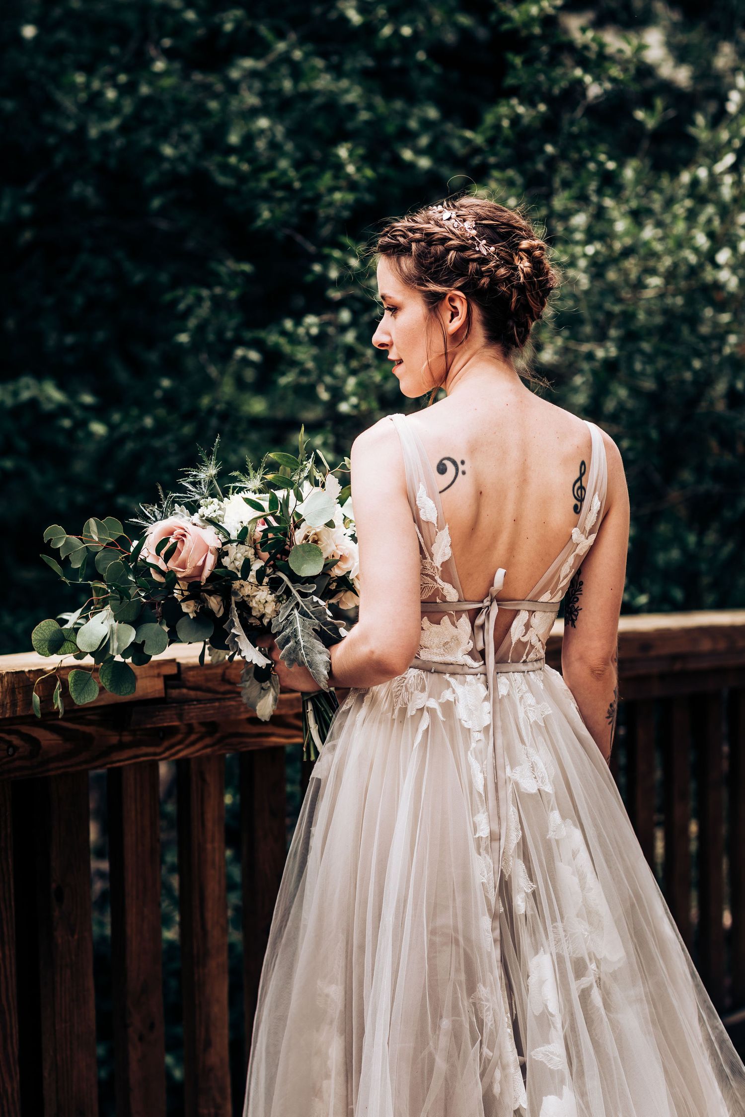 Back view of bride in elegant lace dress holding bouquet showing intricate tattoo details.