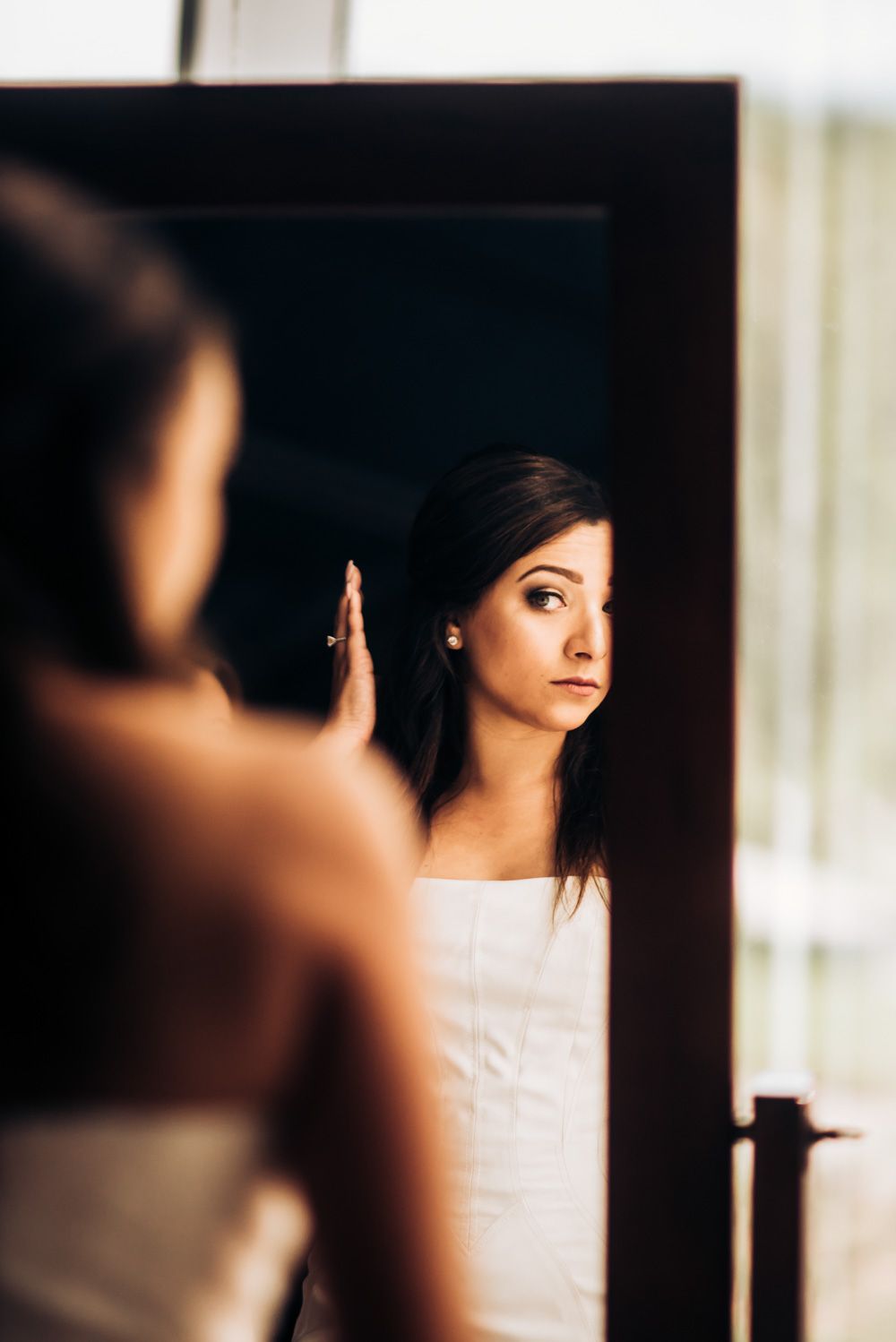 A reflection of someone wearing white in a mirror with a contemplative expression.