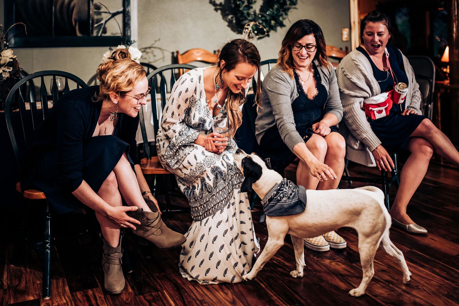 Group interacts with small dog on hardwood floor during indoor celebration.