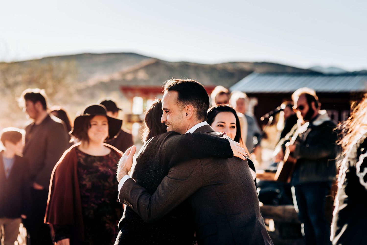 Wedding guests embrace during sunset celebration at outdoor desert venue.