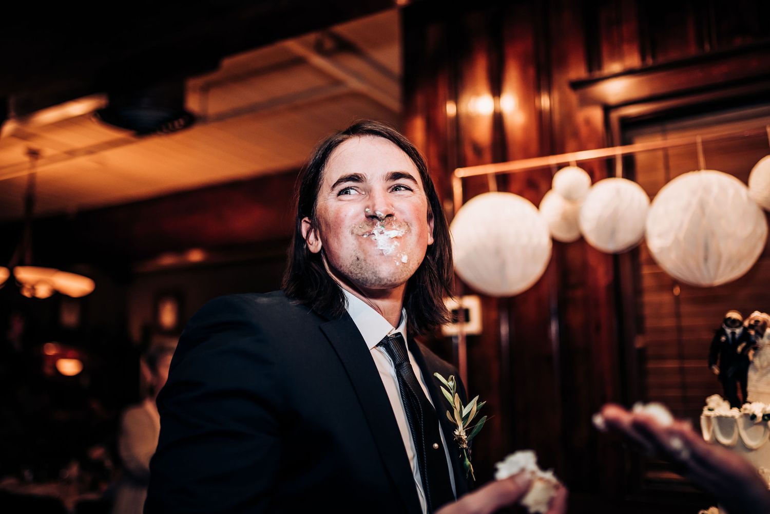 Frosting-covered face laughs during playful wedding cake moment at reception.