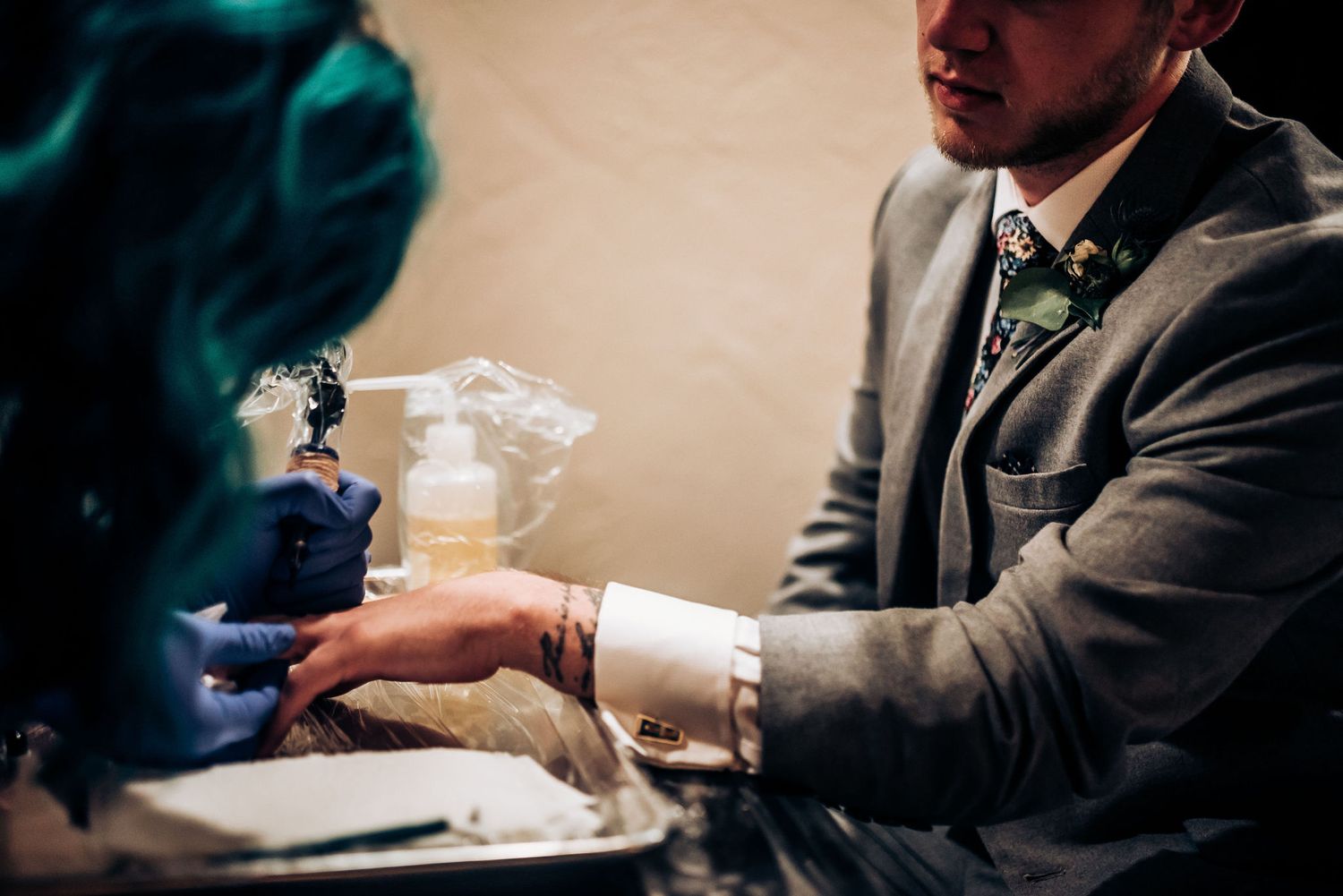 Person in suit jacket receiving tattoo during formal event.
