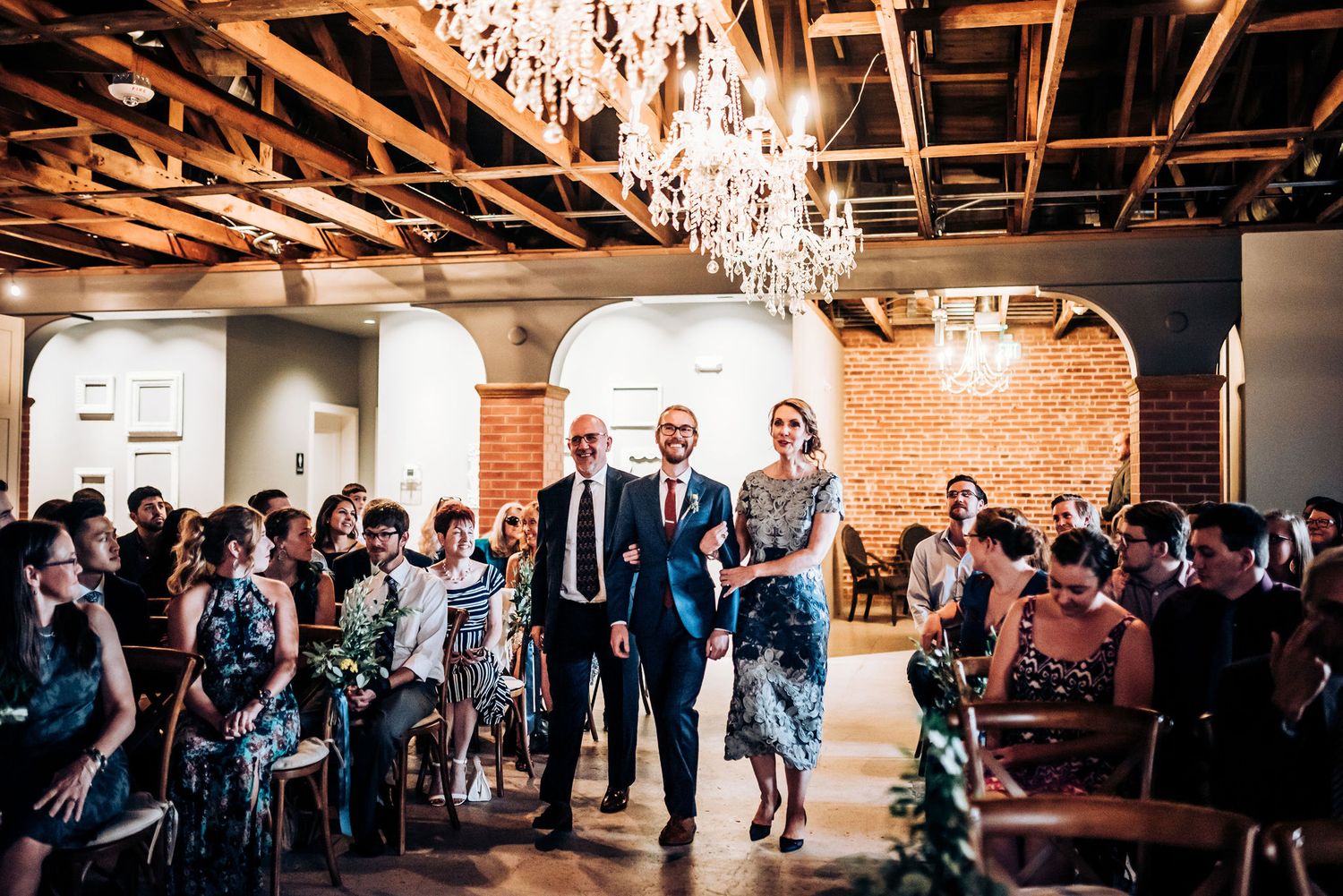 Wedding ceremony processional in an industrial-chic venue with exposed brick and crystal chandeliers.