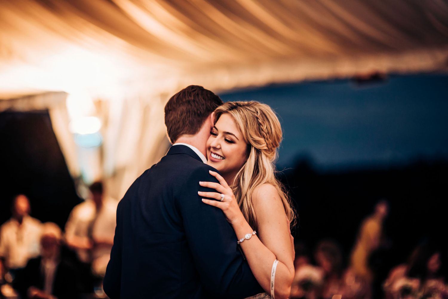 Romantic embrace during first dance at wedding reception under draped tent ceiling.