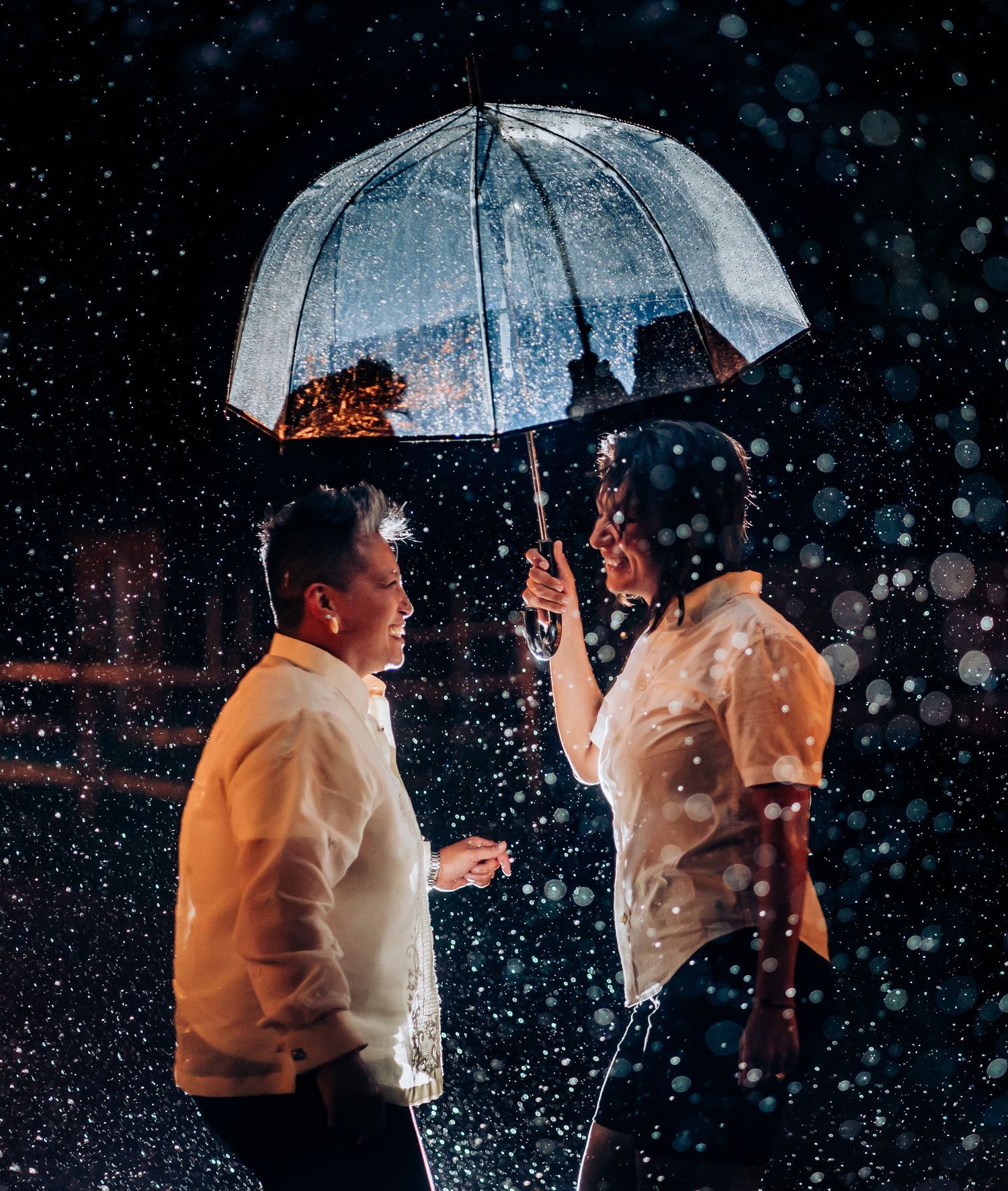 Romantic nighttime photo series with couple under clear umbrella in the rain.