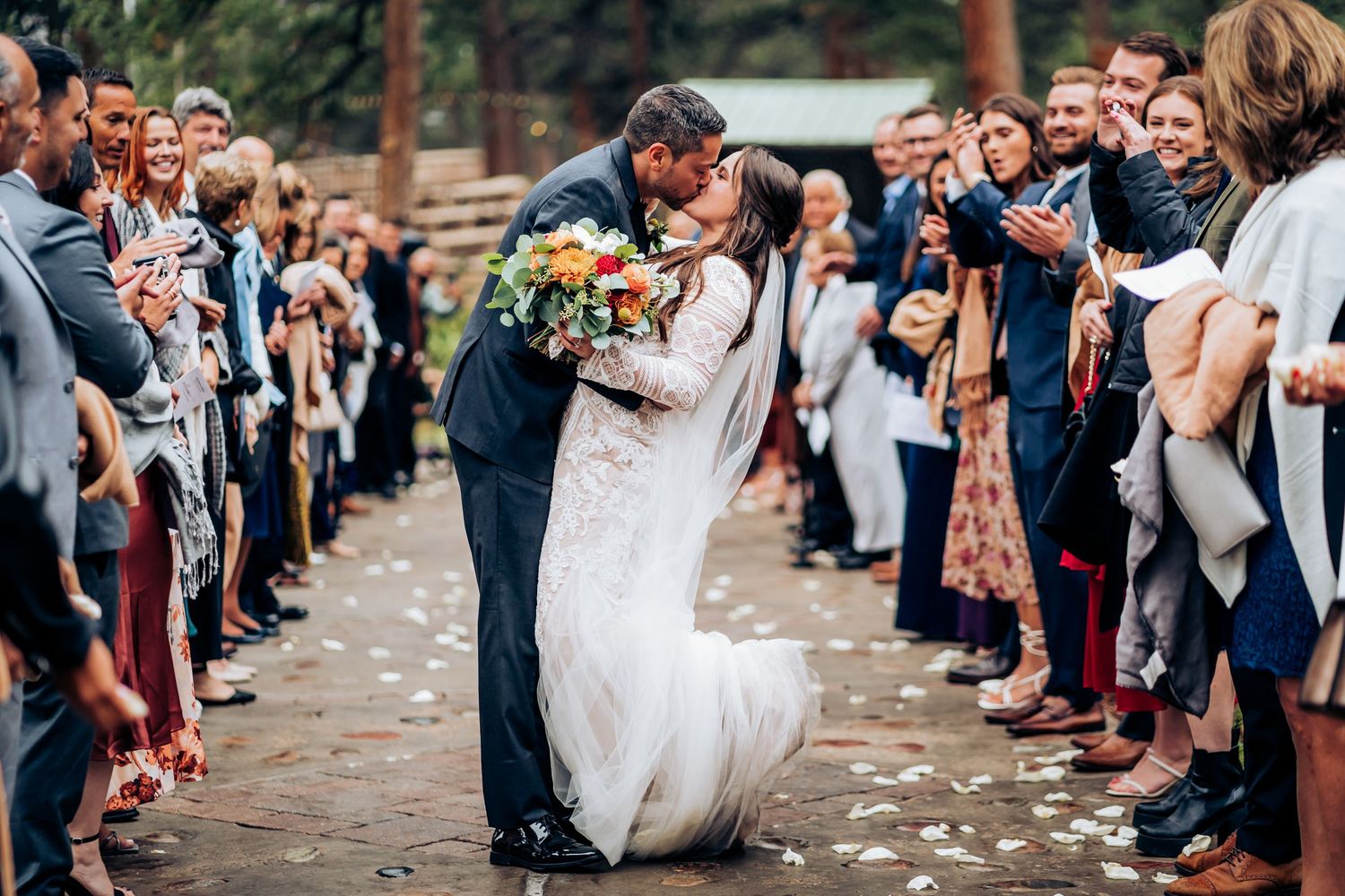 Wedding exit with guests throwing flower petals as couple walks through.