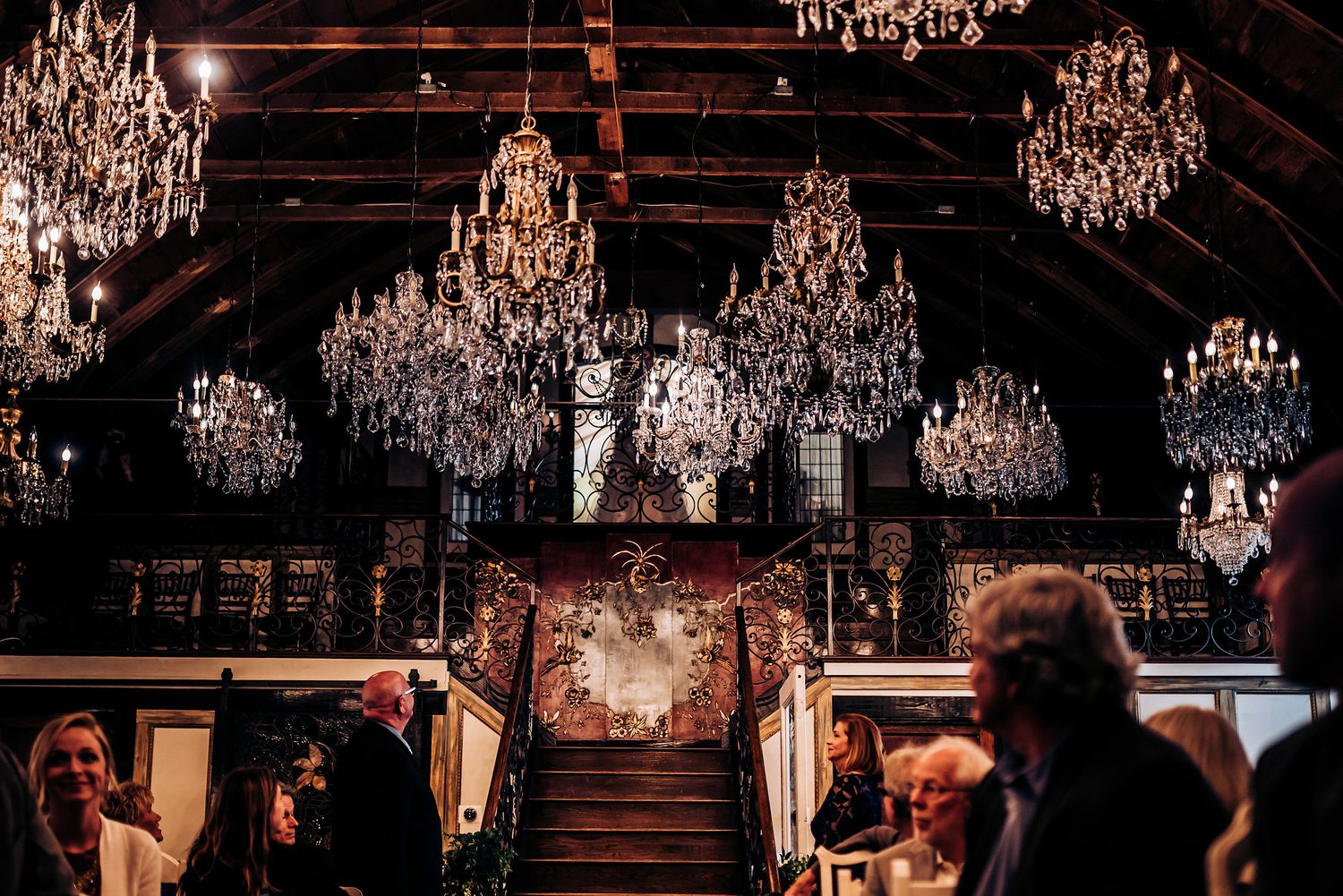 Grand ballroom with stunning crystal chandeliers and elegant staircase during an event.
