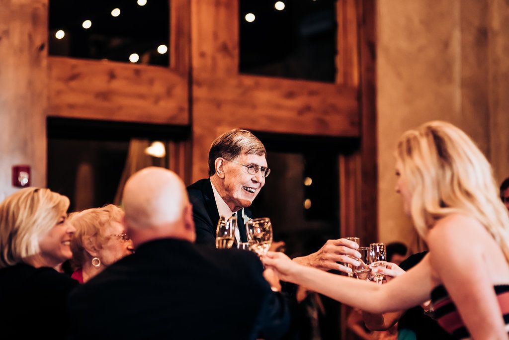 Animated conversation and laughter during wedding reception toast with string lights overhead.