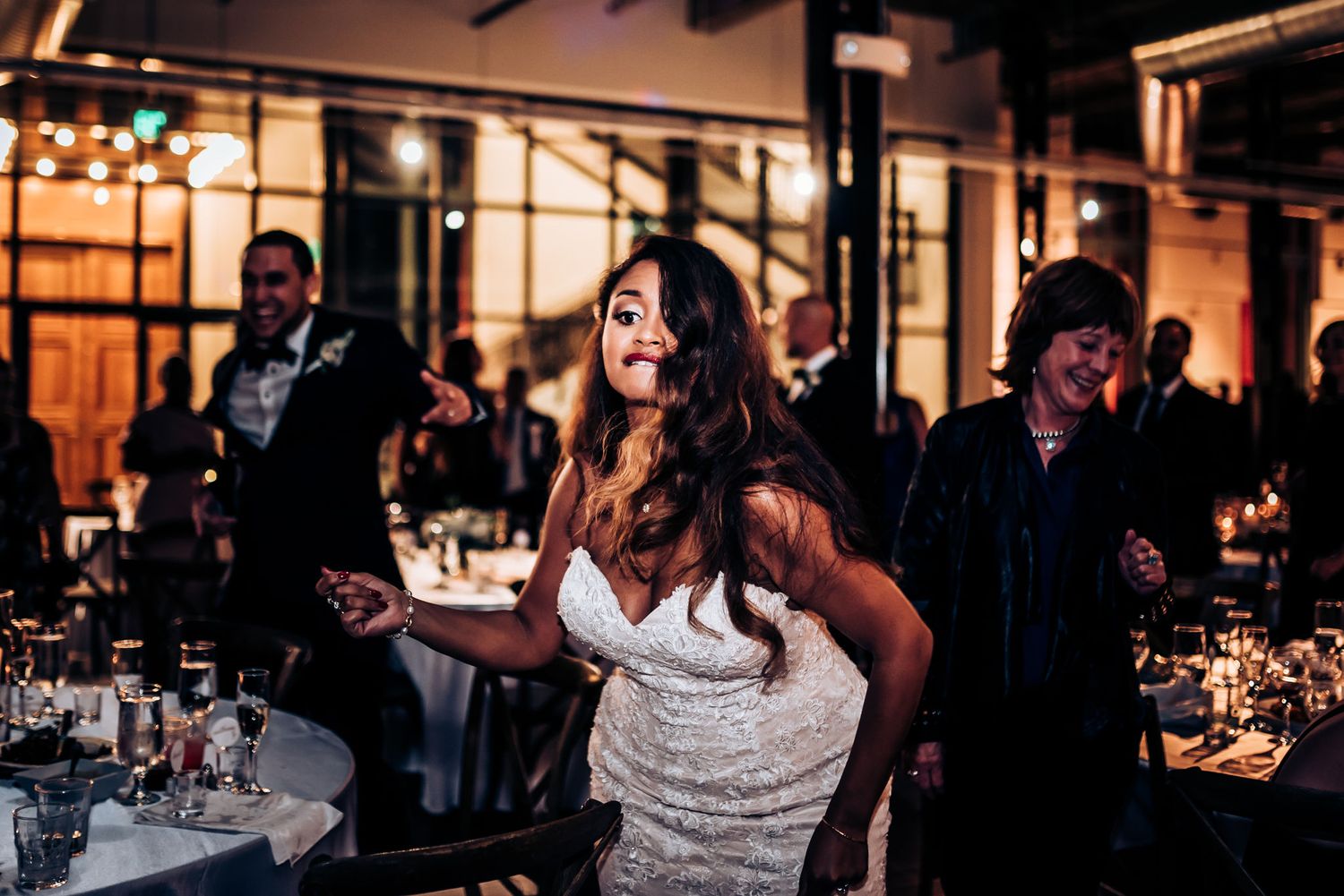 Wedding guests enjoying a lively dance party celebration at an indoor reception venue with ambient lighting.