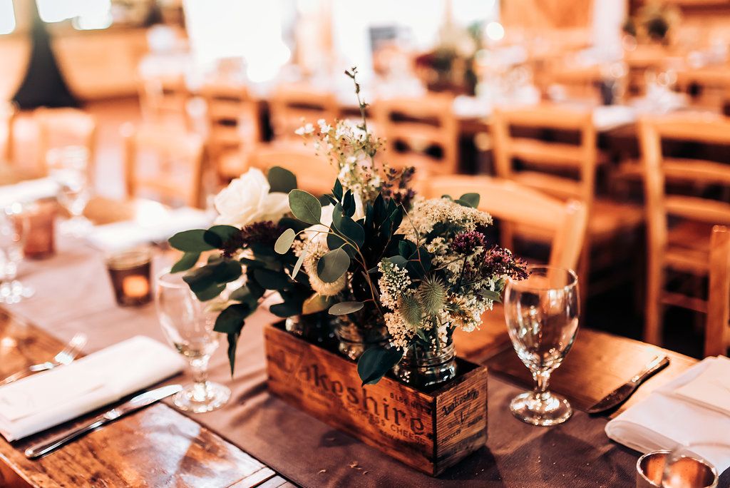 Rustic wooden box centerpiece with fresh greenery and flowers on wedding reception table.