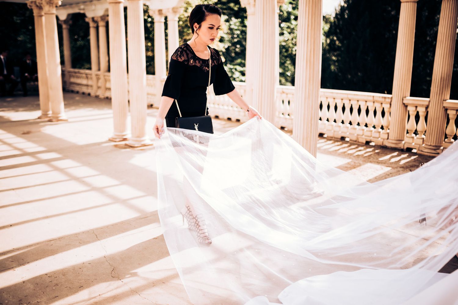 A flowing white wedding veil being arranged on a sunlit porch.