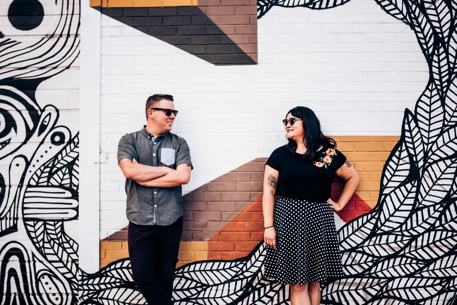 Couple poses against artistic black and white mural wall in urban setting.