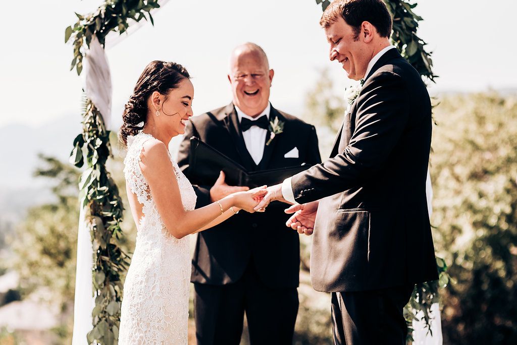 Wedding ceremony exchange of rings under floral arch with mountain vista.