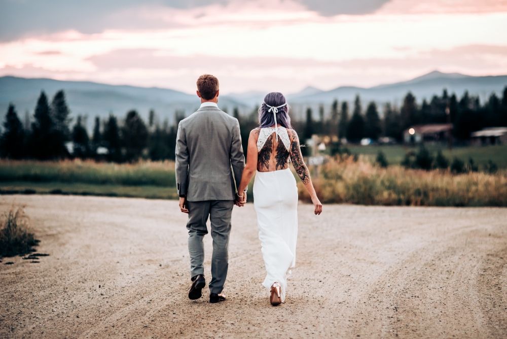 A couple walks down a dirt road with mountains and pine trees in the distance.
