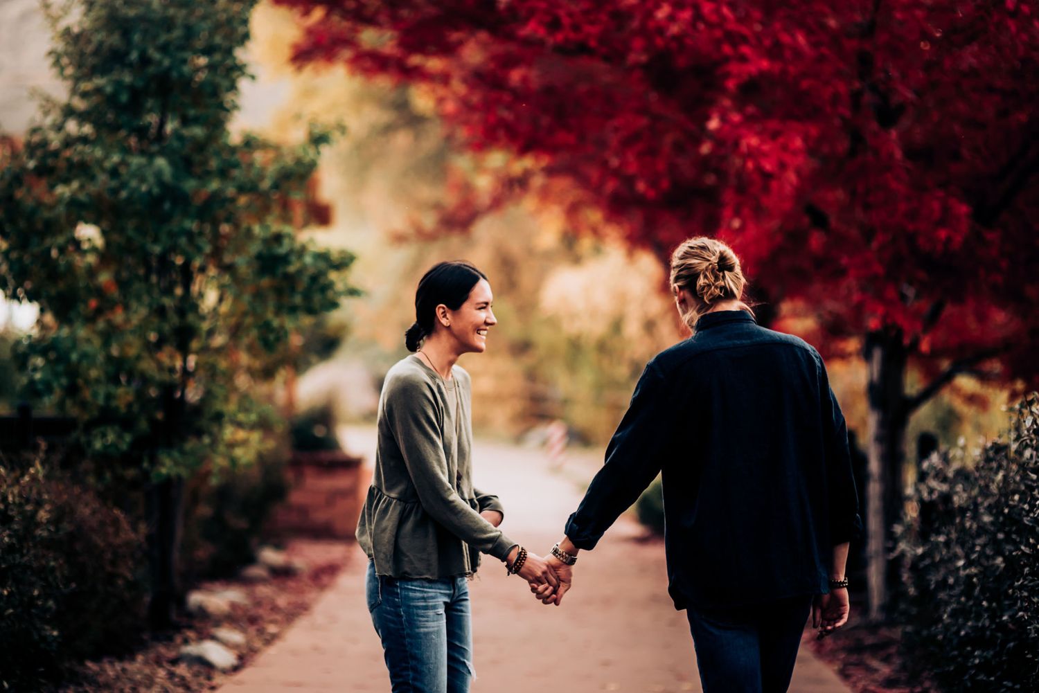 A couple walking hand in hand down a path surrounded by vibrant fall foliage.