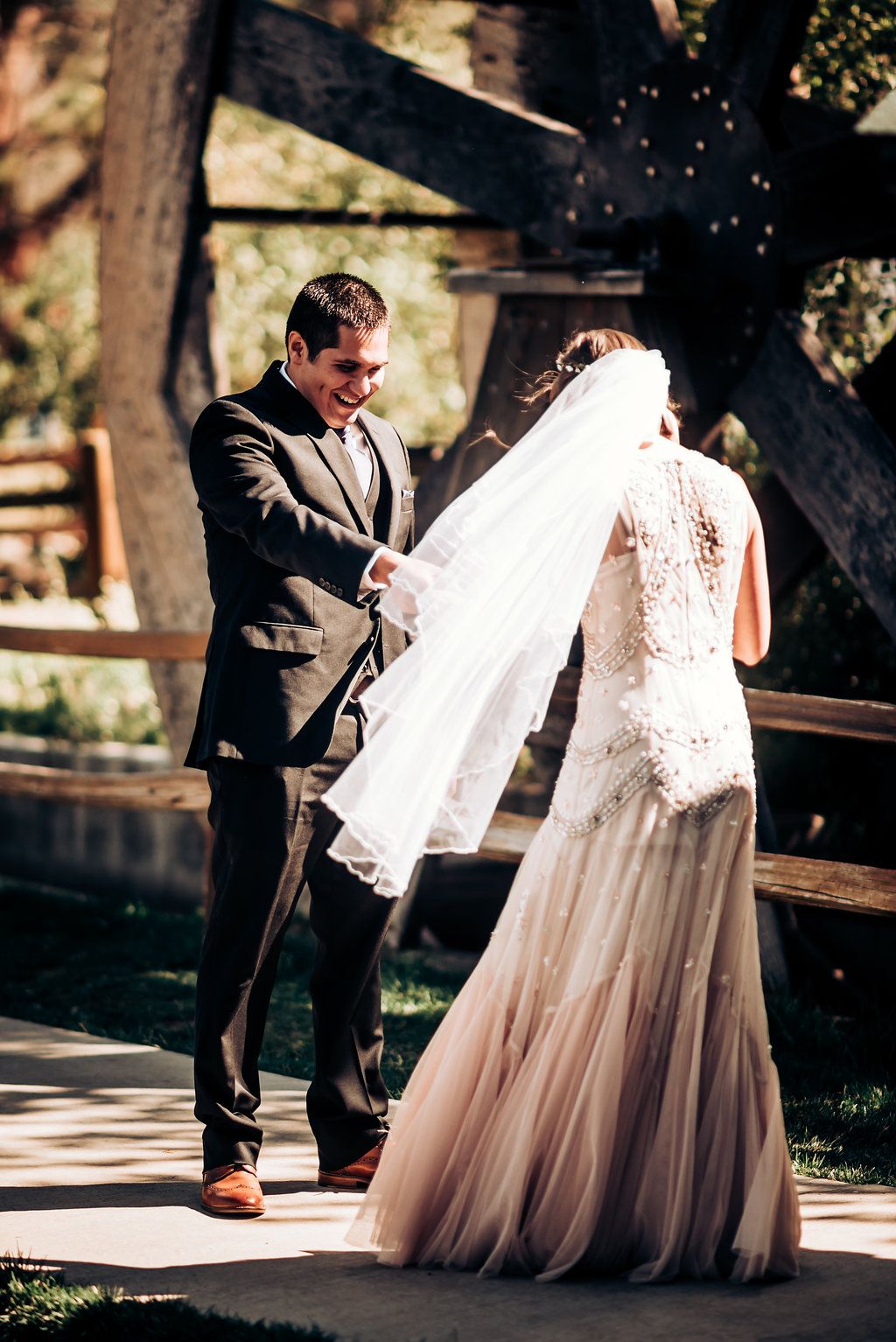 Wedding couple shares a tender moment on a wooden deck in dappled sunlight.