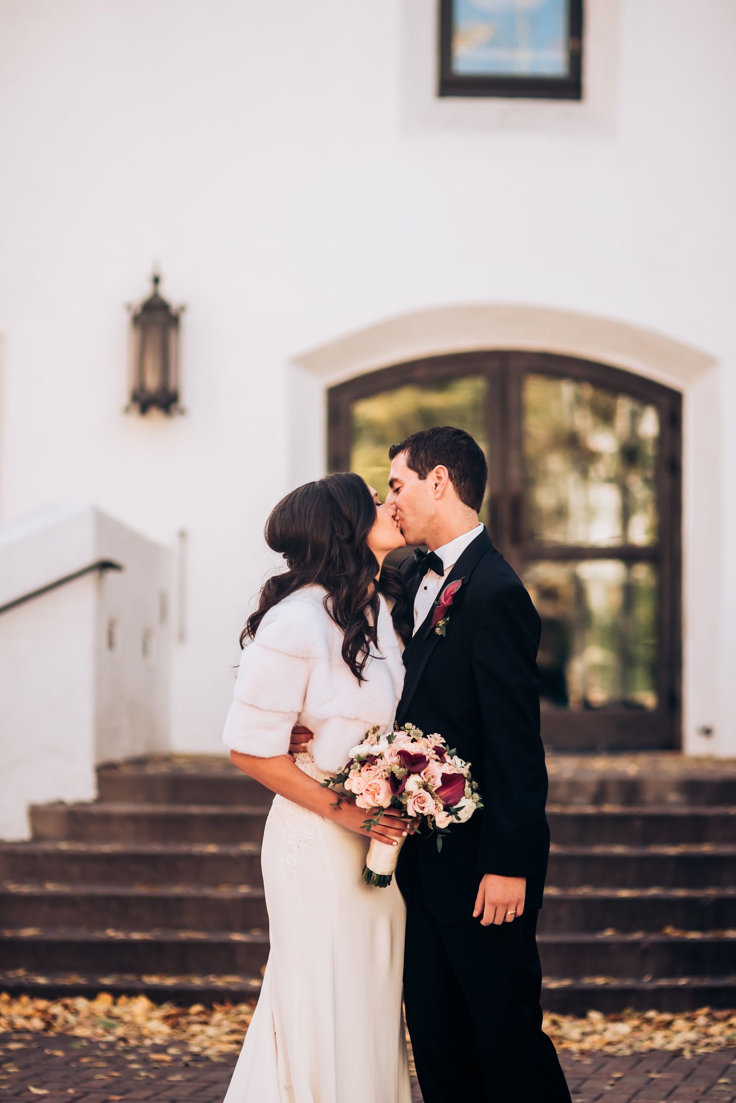 Romantic wedding portrait of couple sharing intimate moment on church steps with autumn leaves.