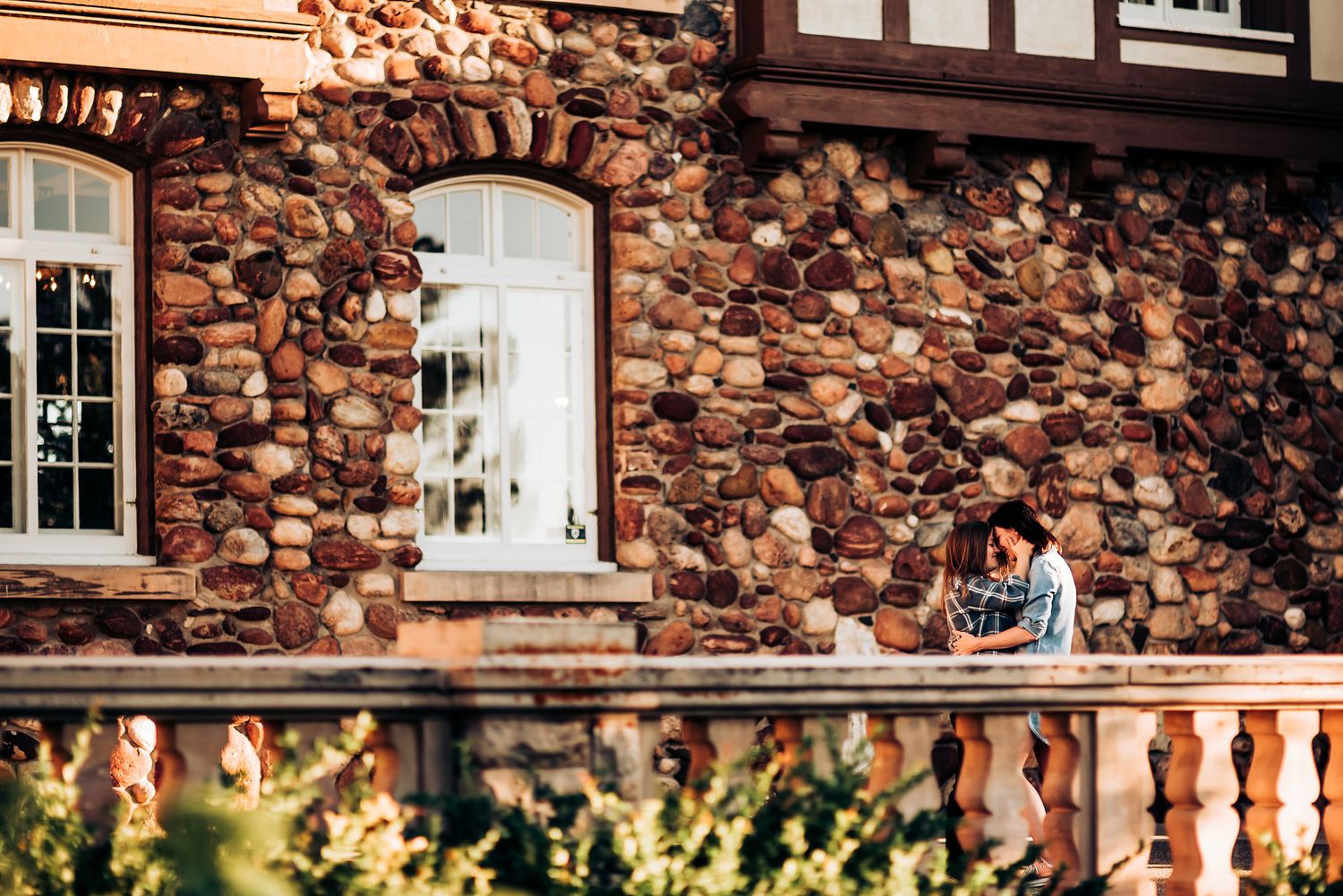 Couple sitting together against rustic stone wall with arched windows.