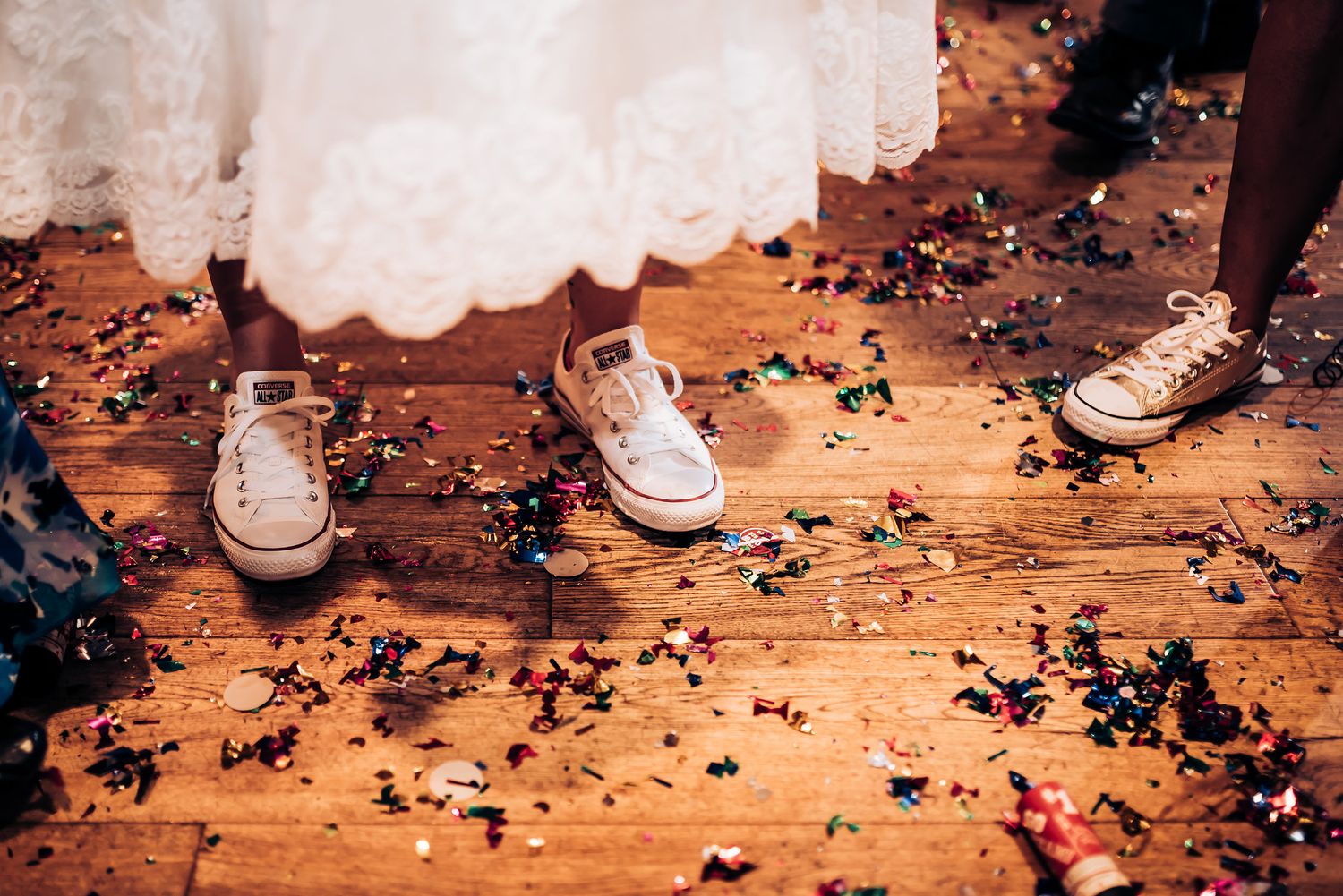 White sneakers on wooden floor with scattered confetti at wedding reception.
