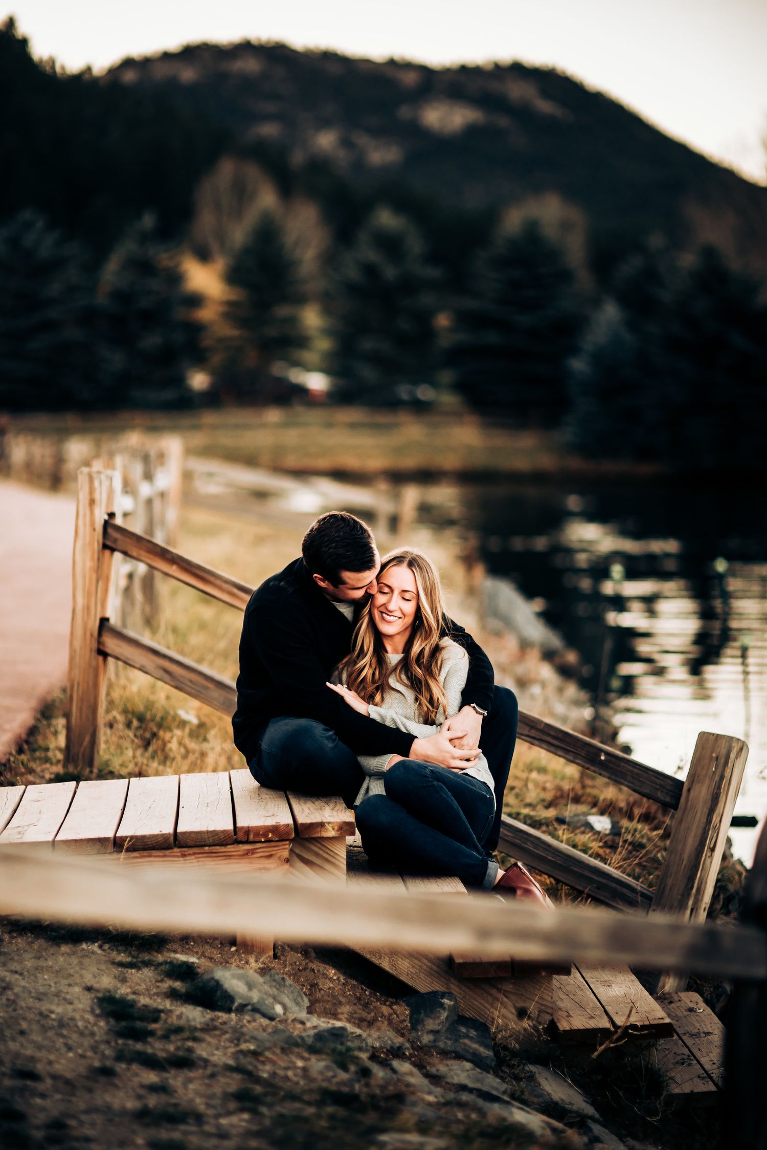 Couple cuddling on wooden dock by mountain lake at sunset.