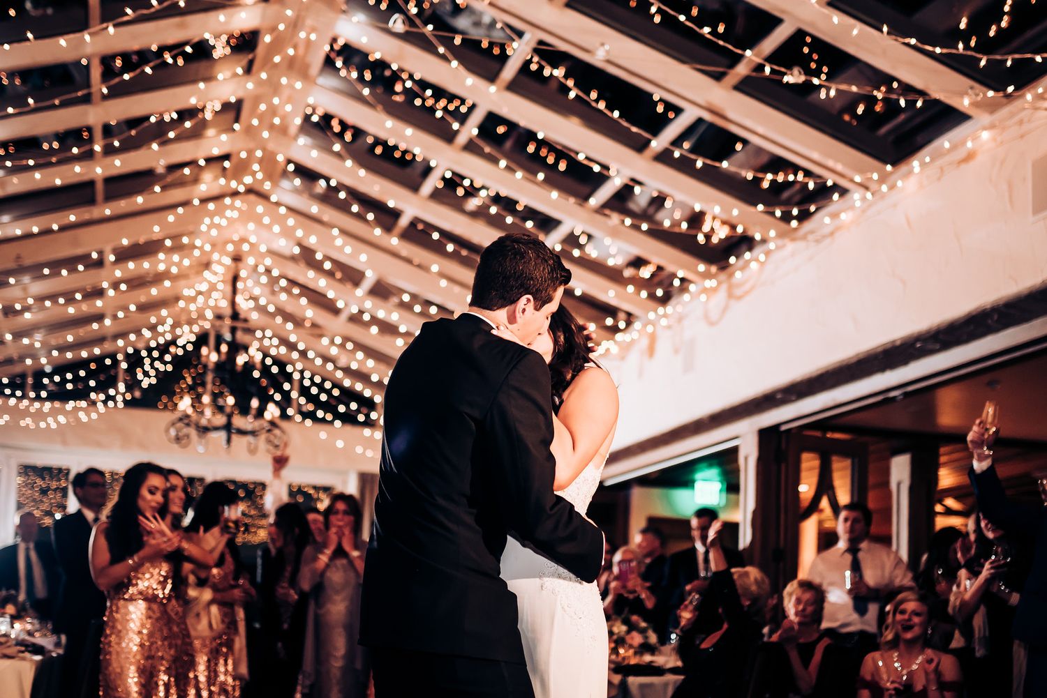Newlyweds share their first dance under twinkling string lights in an elegant reception venue.