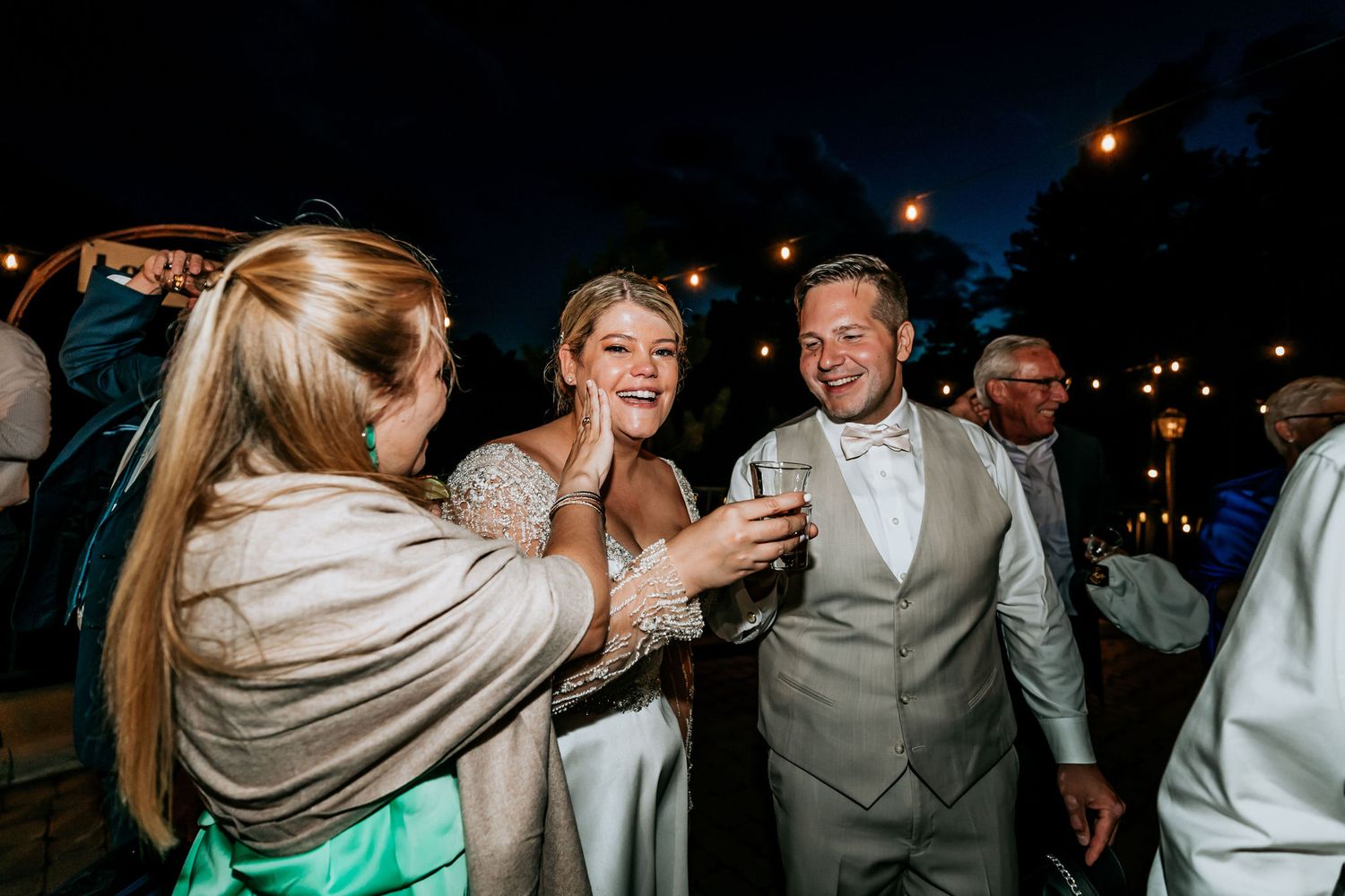 Wedding celebration with guests toasting and enjoying drinks at an outdoor evening reception.