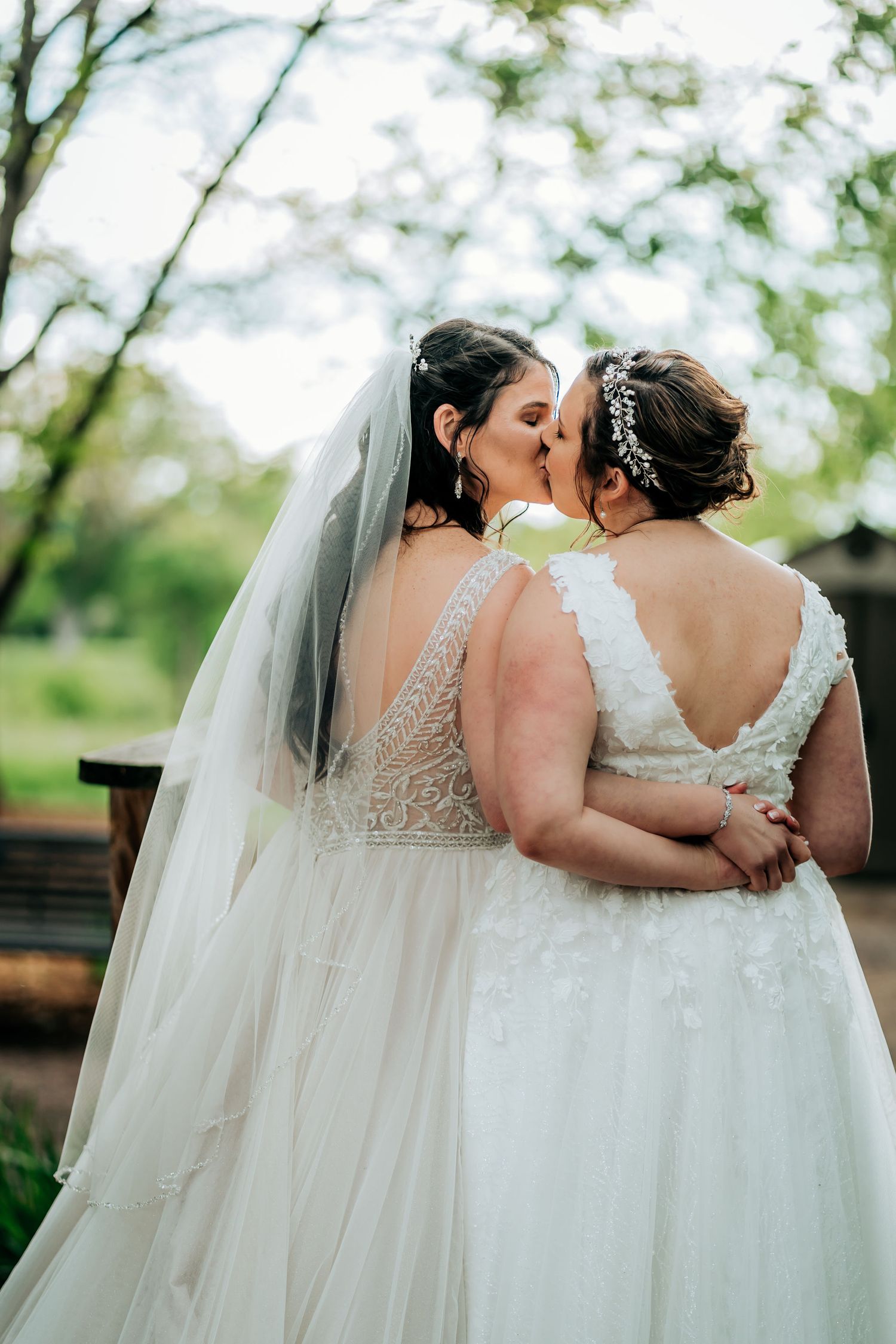 Two brides in white wedding dresses sharing an intimate moment outdoors.