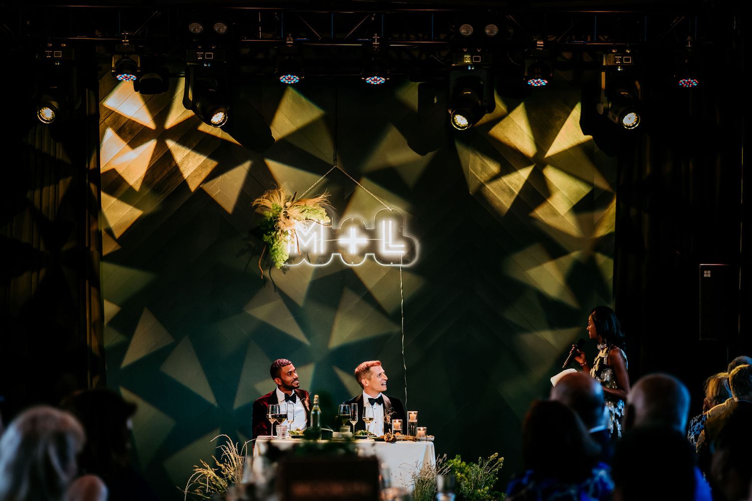 Wedding reception venue with geometric backdrop lighting and decorative stage setup.