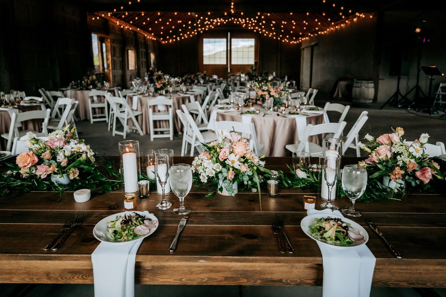 Rustic barn wedding reception setup with string lights and elegant table settings.