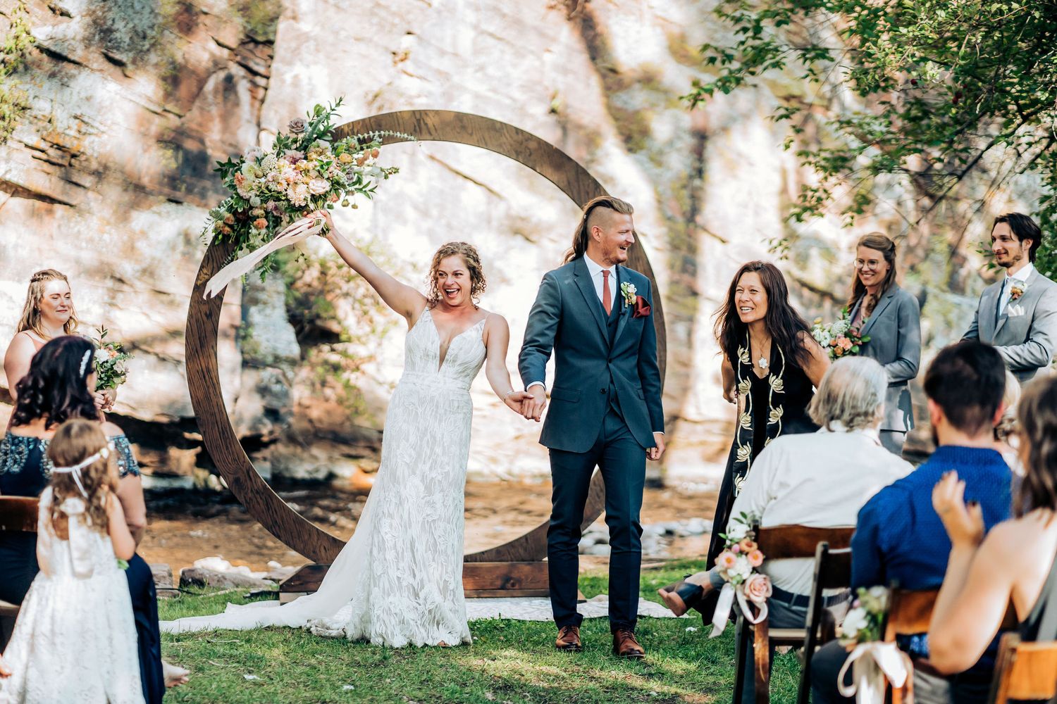 Wedding celebration with guests watching couple celebrate under circular arch at outdoor venue.