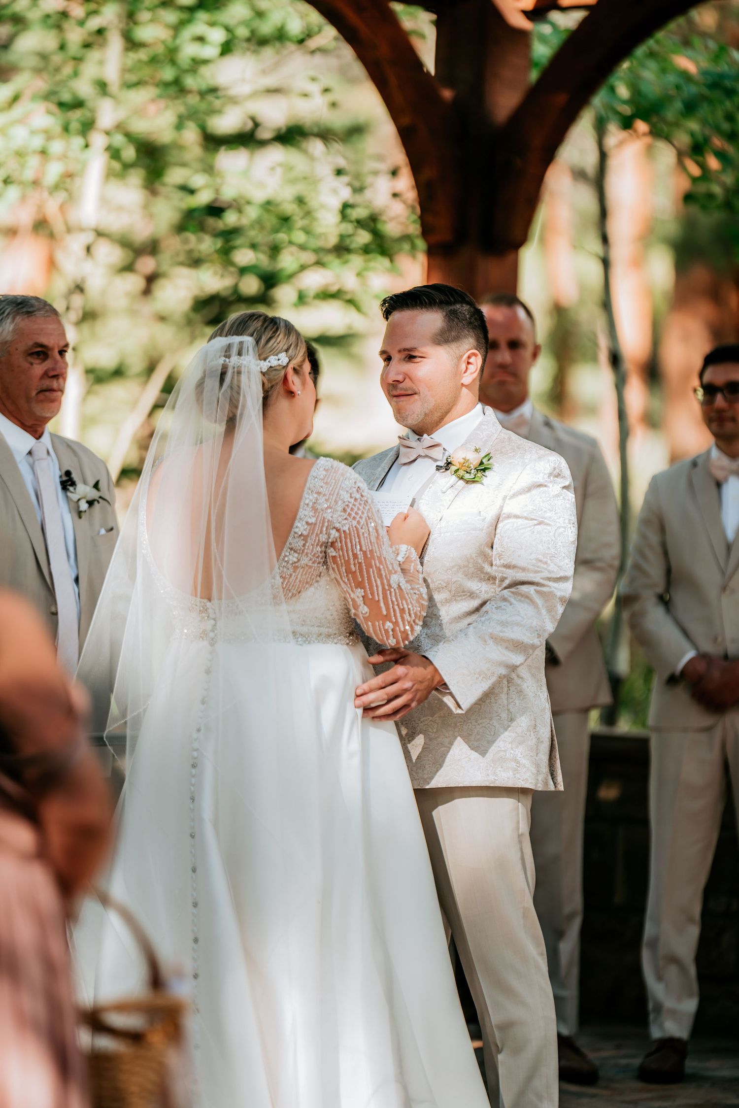 An emotional wedding ceremony taking place under a rustic wooden arch outdoors.