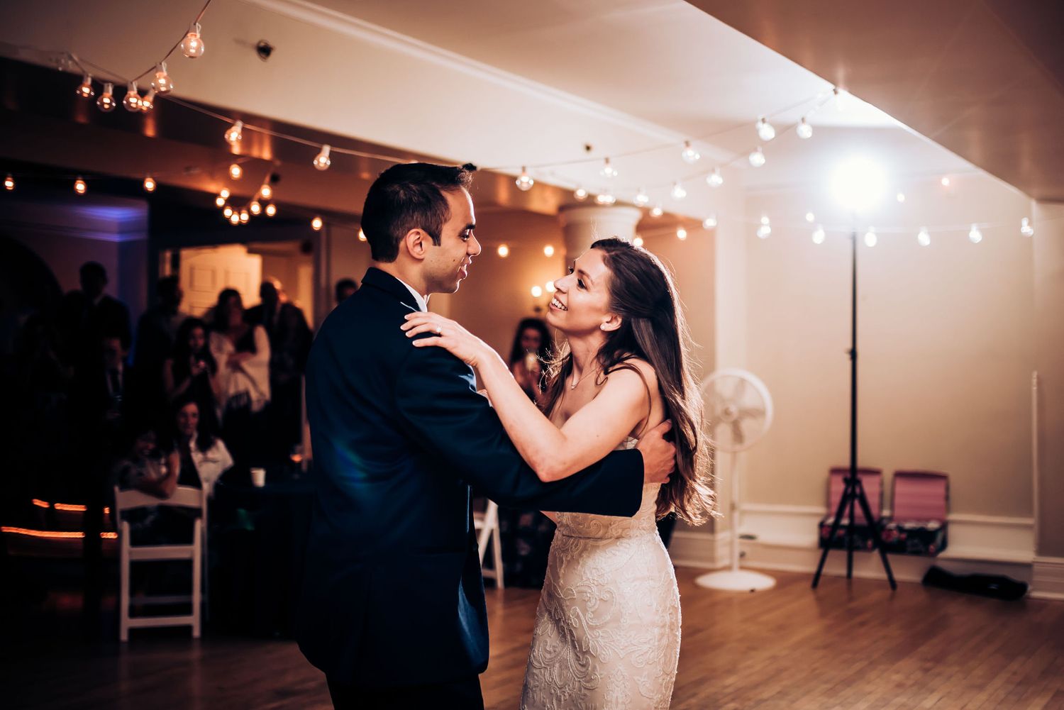 A couple shares a romantic dance moment under twinkling lights at their reception.
