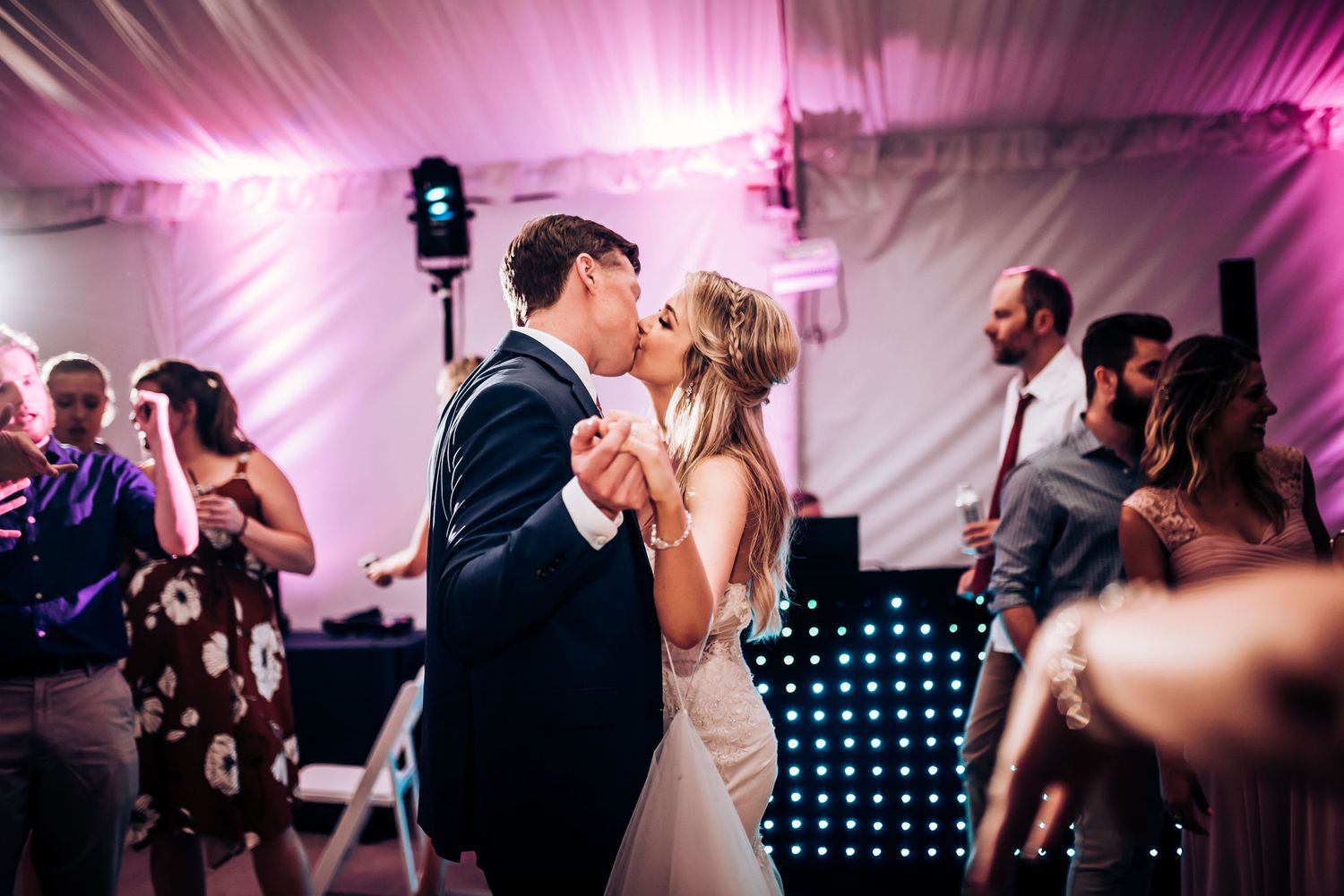 Couples dancing on the reception floor with purple lighting and a DJ booth in the background.