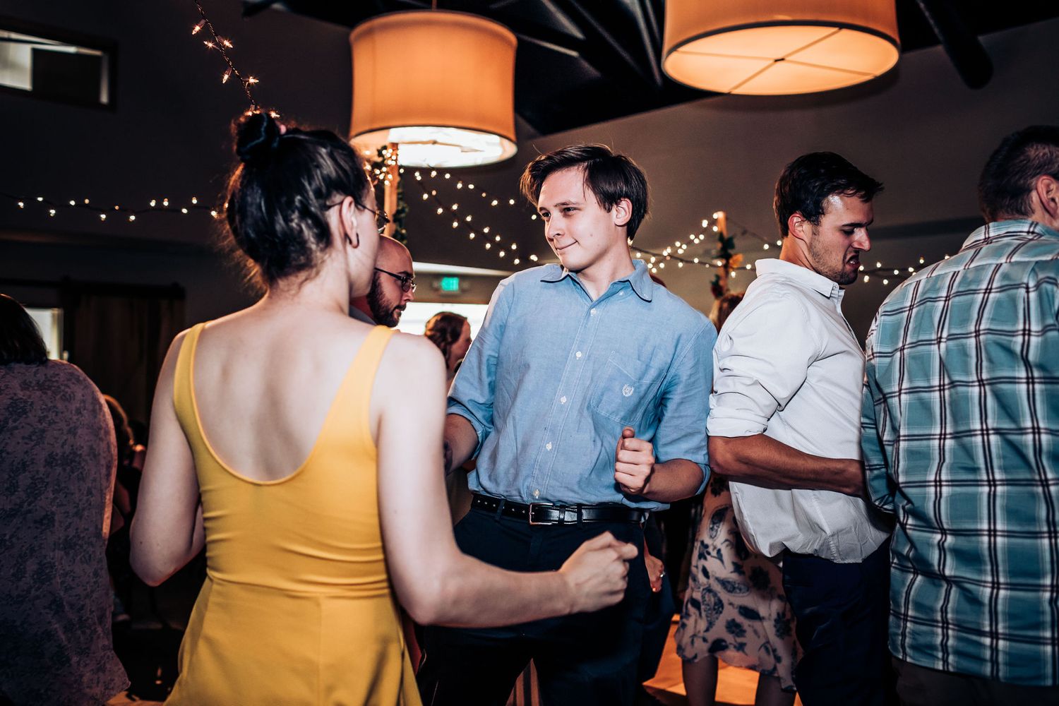 Casual reception gathering with guests mingling under pendant lights and string lighting.