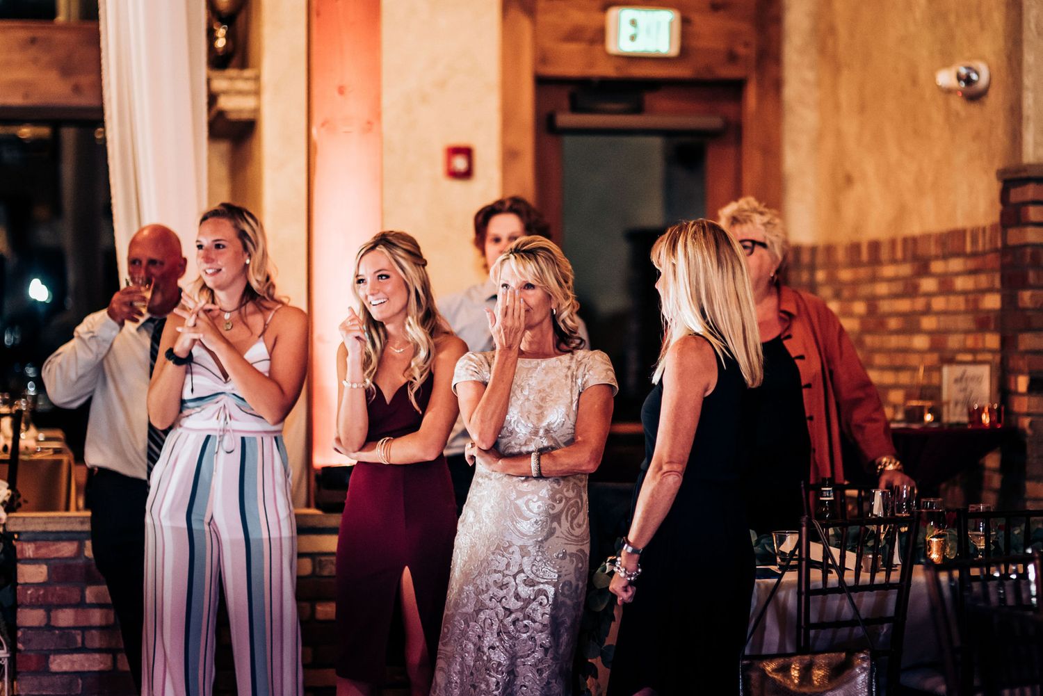 Wedding guests react emotionally during a reception moment in an indoor venue.