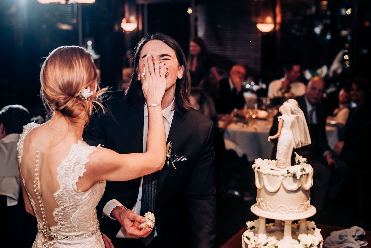 Playful cake cutting moment at wedding reception with elegant tiered cake in background.