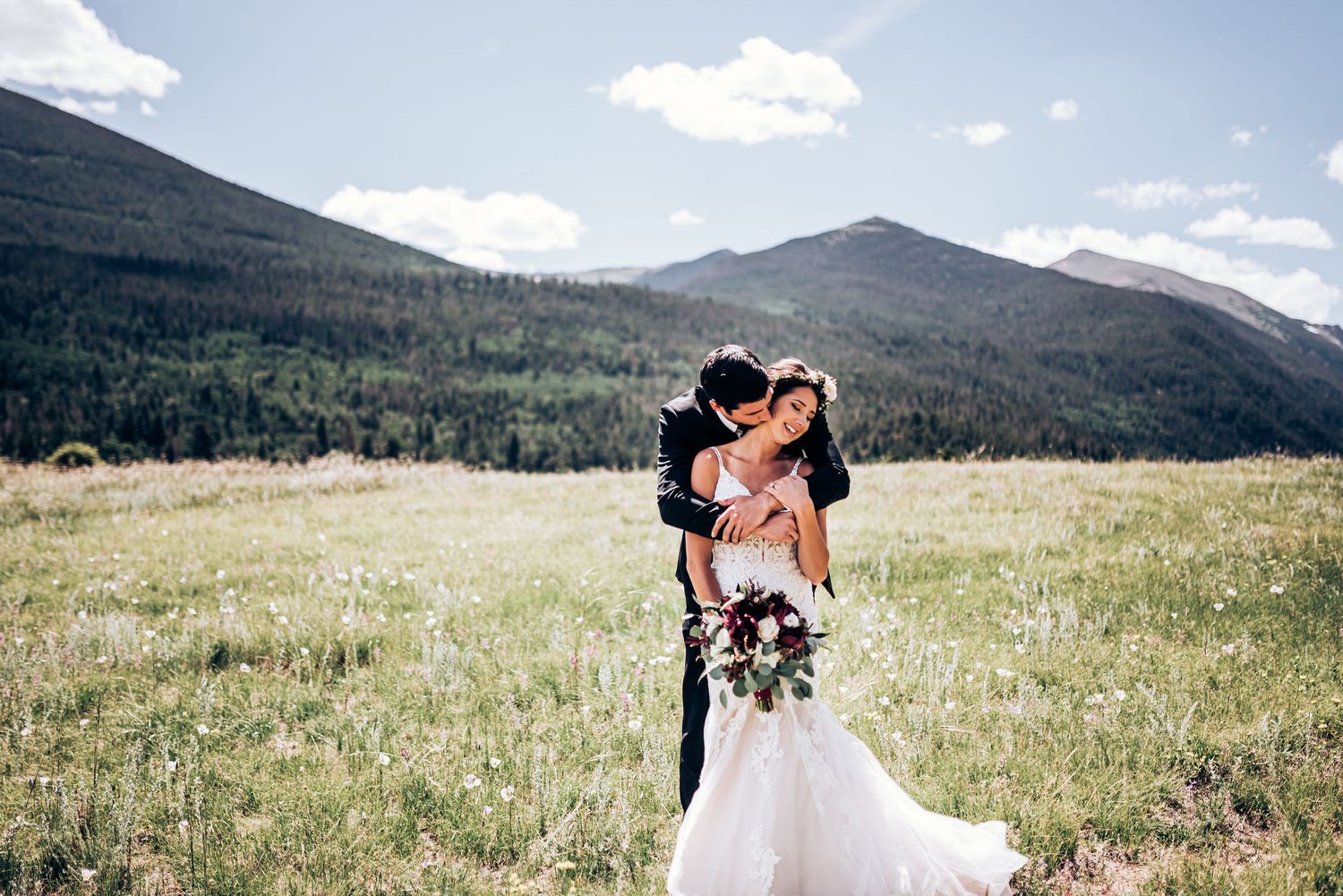 A tender wedding moment captured in a mountain meadow under blue summer skies.