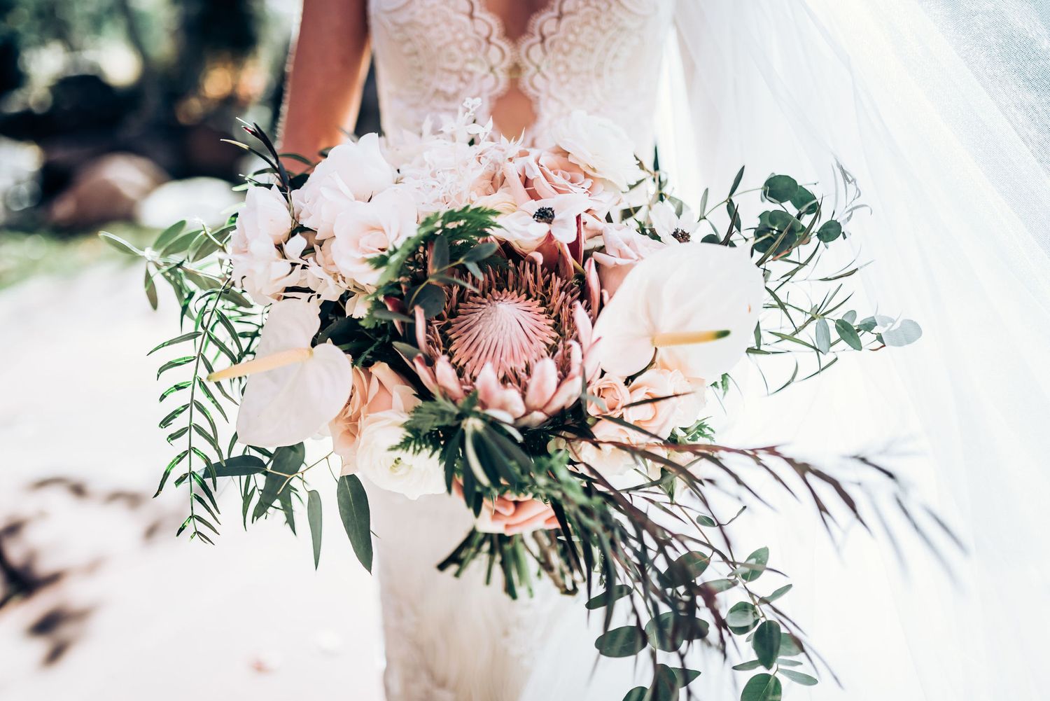 Close-up of a romantic bridal bouquet featuring pink protea and eucalyptus greenery.