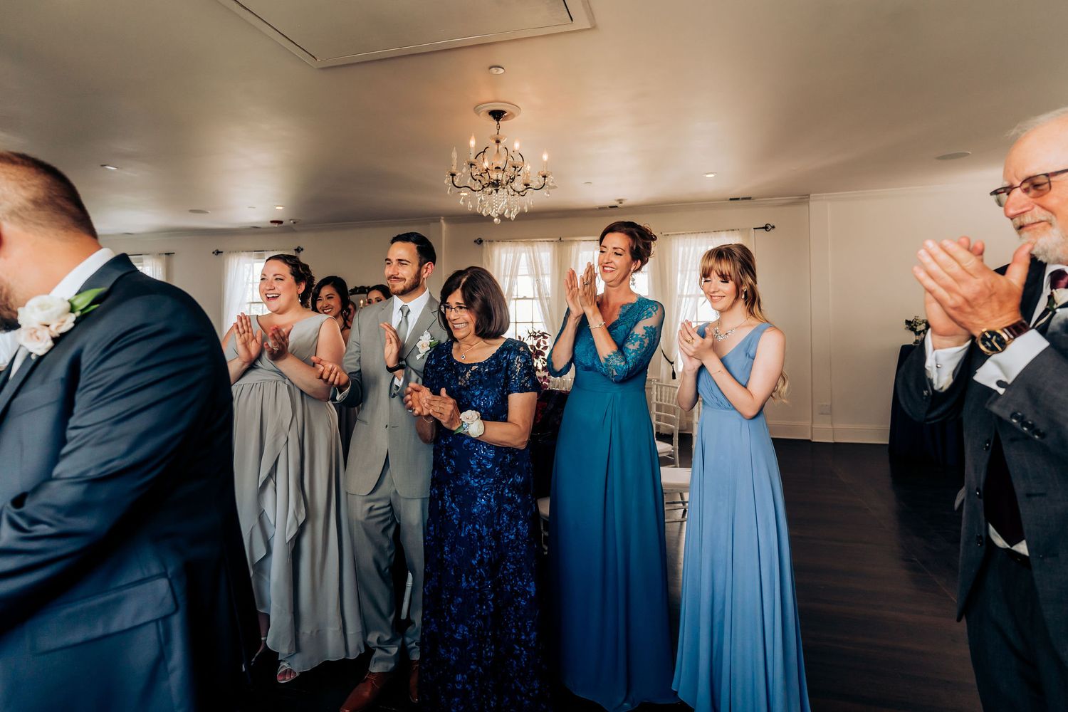 Wedding guests in formal attire applauding during indoor ceremony.