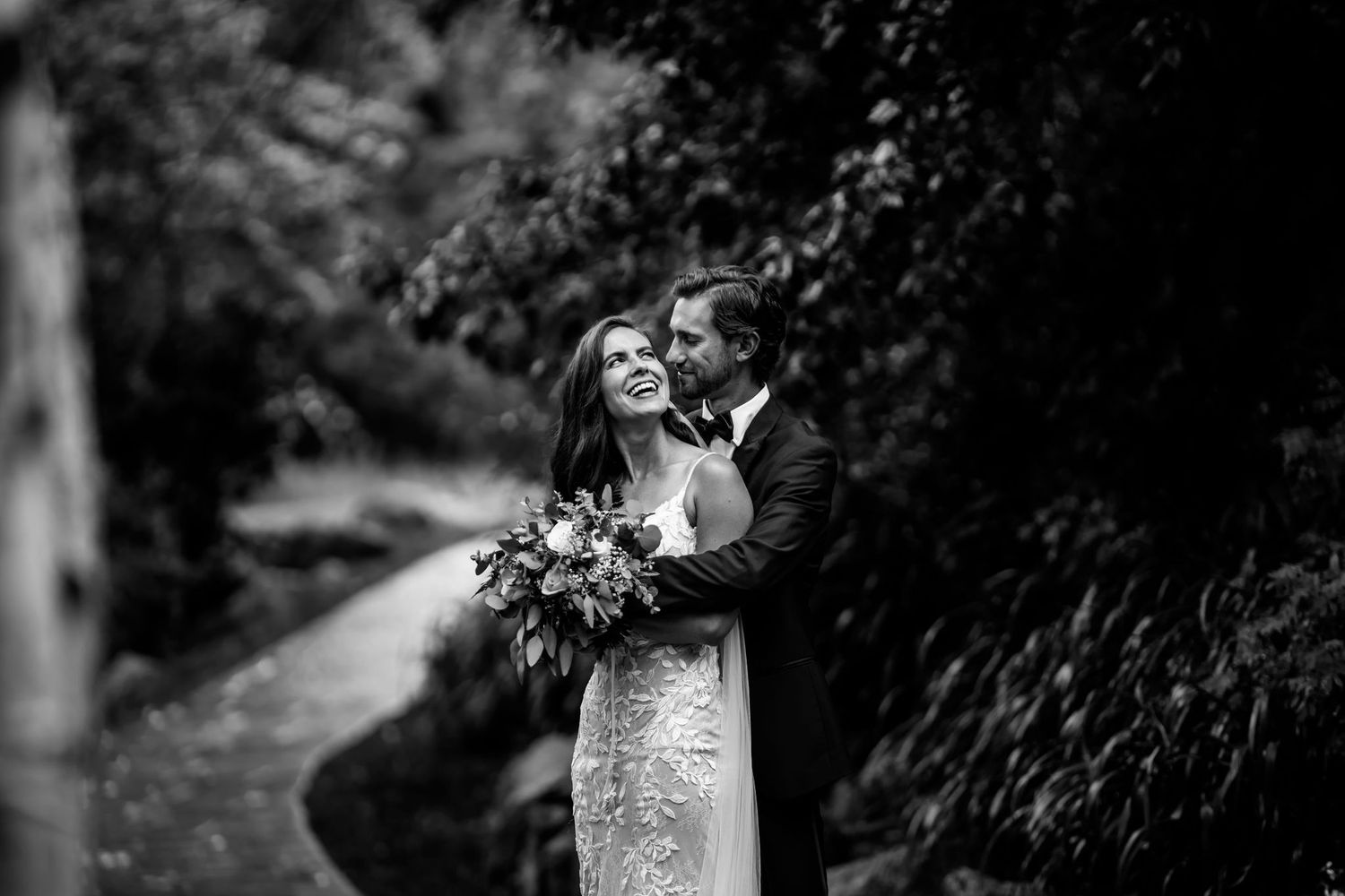 A romantic black and white portrait of newlyweds sharing an intimate moment in a garden setting.