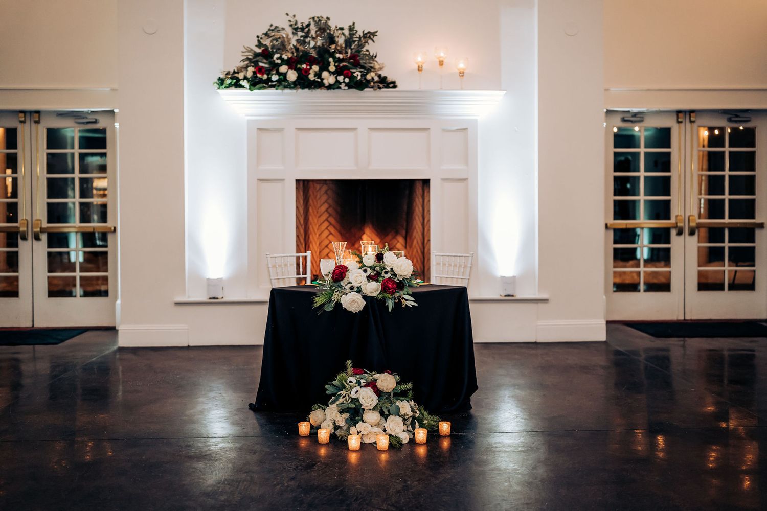 Elegant white fireplace decorated with floral arrangements and candles for a wedding reception.