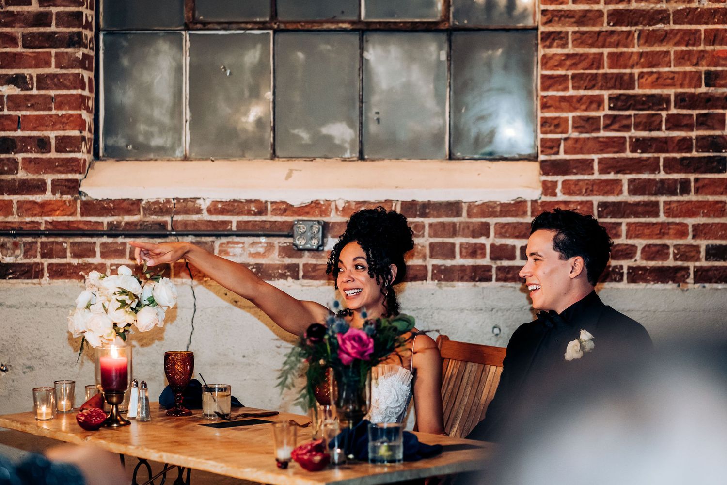 A speaker gestures animatedly during a wedding reception toast in an industrial-style venue.