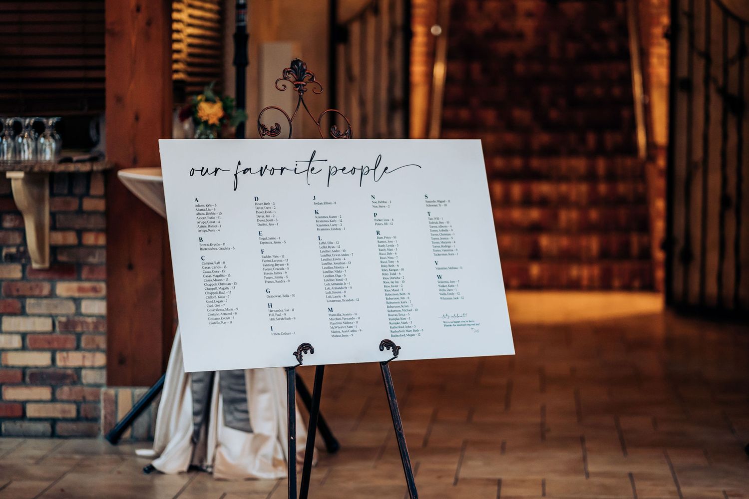 A wedding seating chart displayed on an easel at a rustic venue entrance.