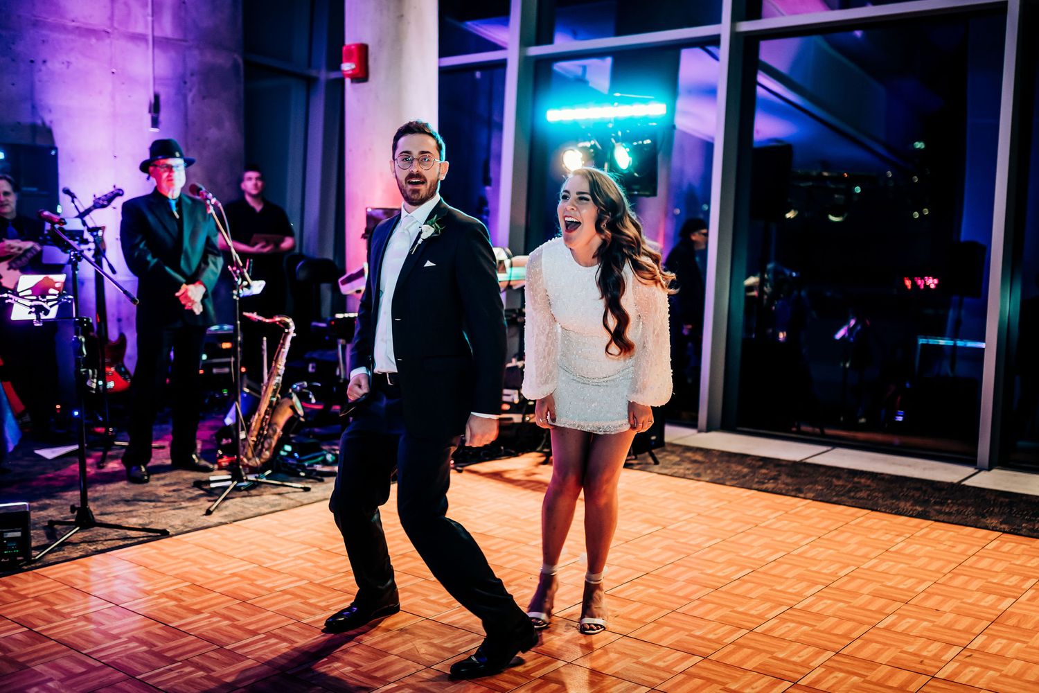 Two people dance enthusiastically on a wooden floor with blue neon lighting in background.