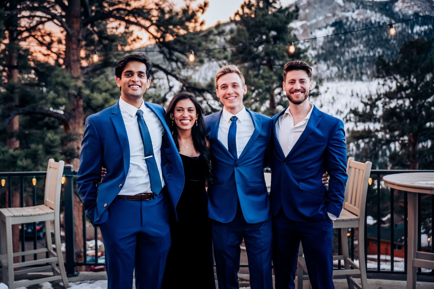 Wedding party in blue suits posed together on mountain deck during sunset.