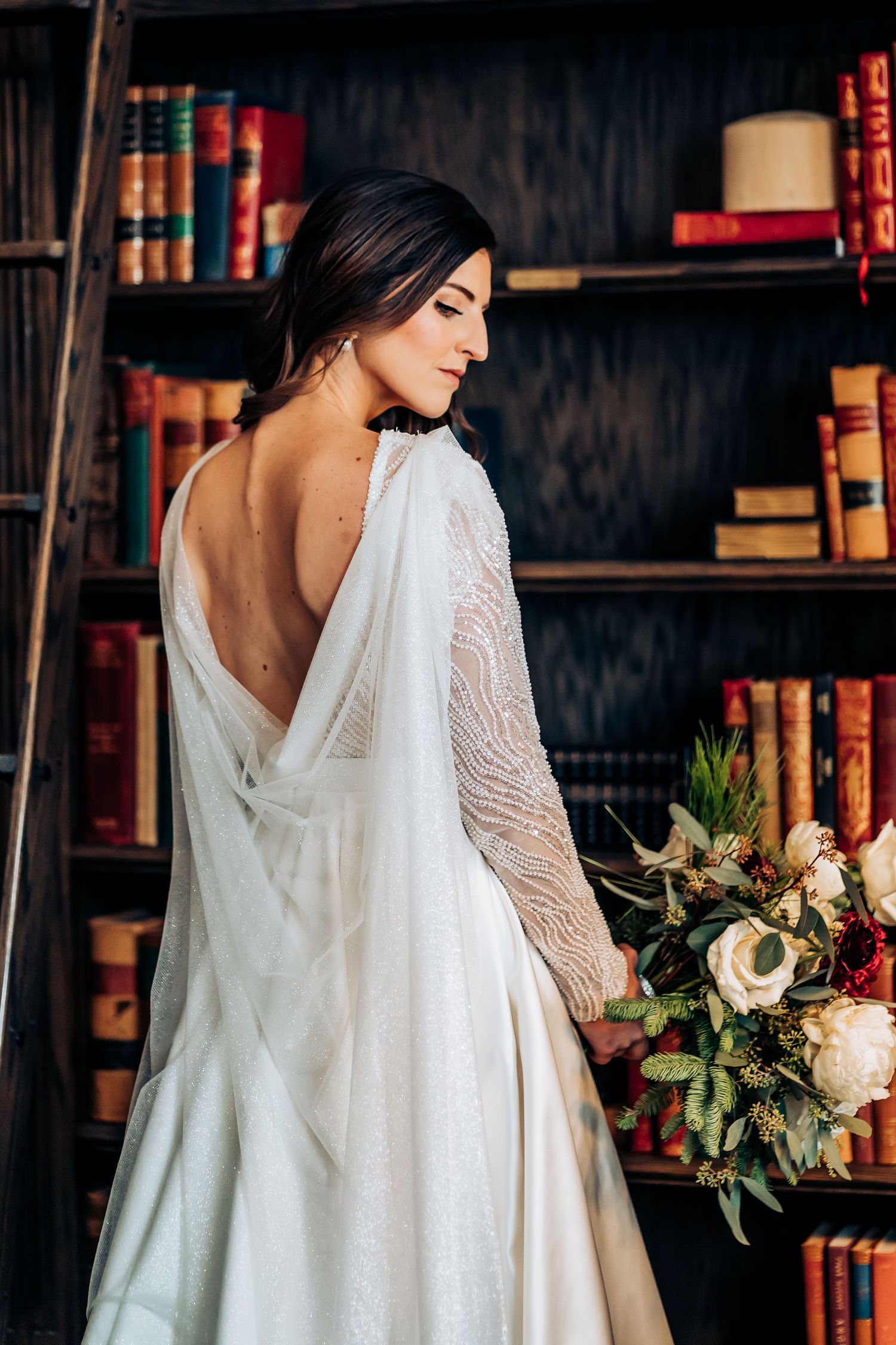 Elegant bridal portrait showing backless wedding dress detail in library setting.